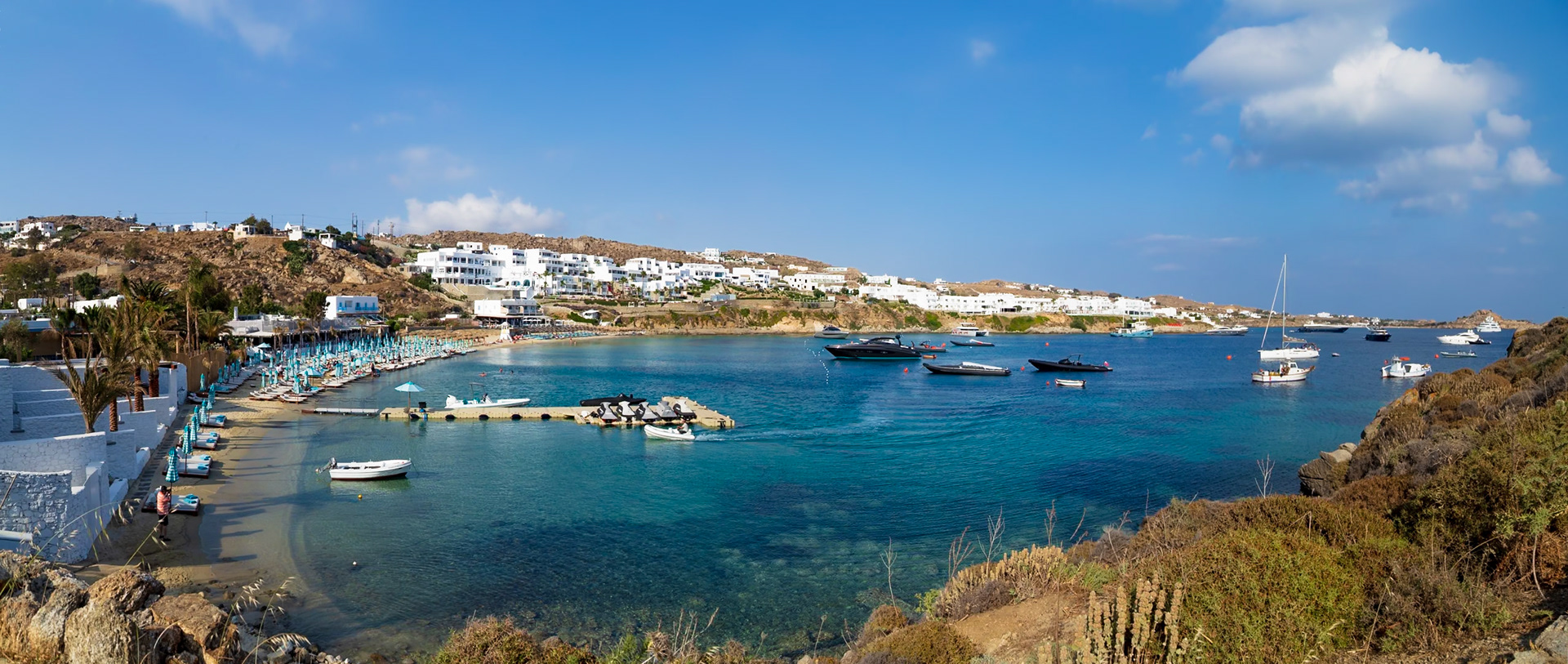 Psarou Beach, Mykonos, Greece - May 24th 2018: A scenic view of the beach with boats, yachts, and white buildings, capturing the essence of a Greek island getaway.