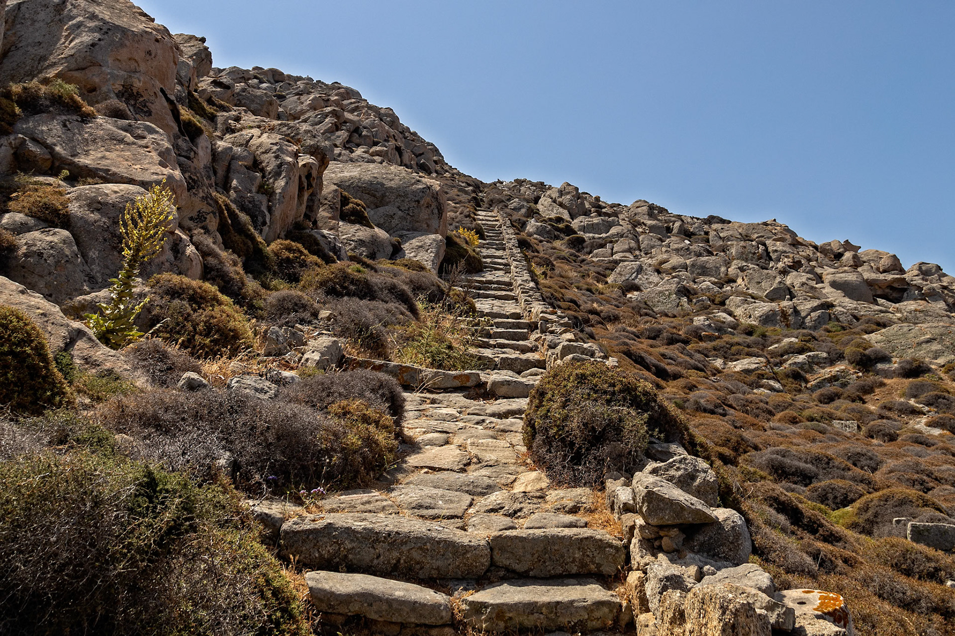 Delos, Greece - May 22nd 2018: A stone path leads up a rocky hillside, likely used by visitors exploring the ancient ruins and natural landscape of the island.