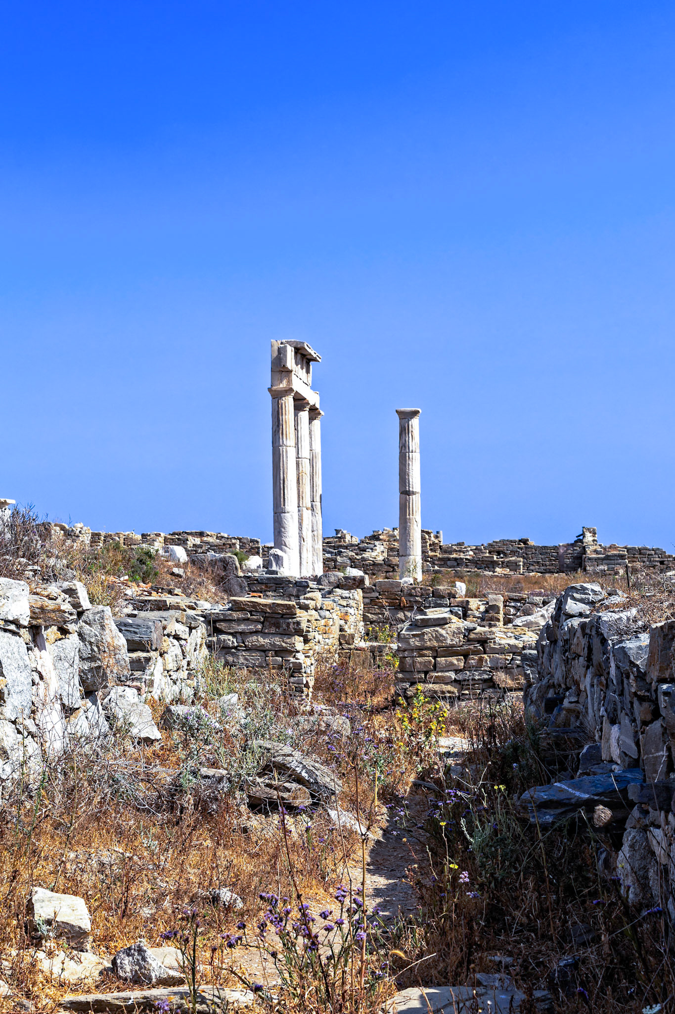 Delos, Greece - May 22nd 2018: Ruins of the Temple of Apollo stand tall against a clear blue sky. The site is a popular tourist destination for its historical significance.