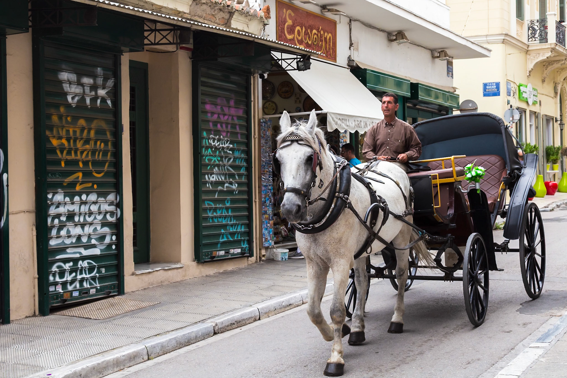 Athens, Greece - May 23rd 2018: A horse-drawn carriage, driven by a man, travels down a street, offering a traditional mode of transport for tourists.