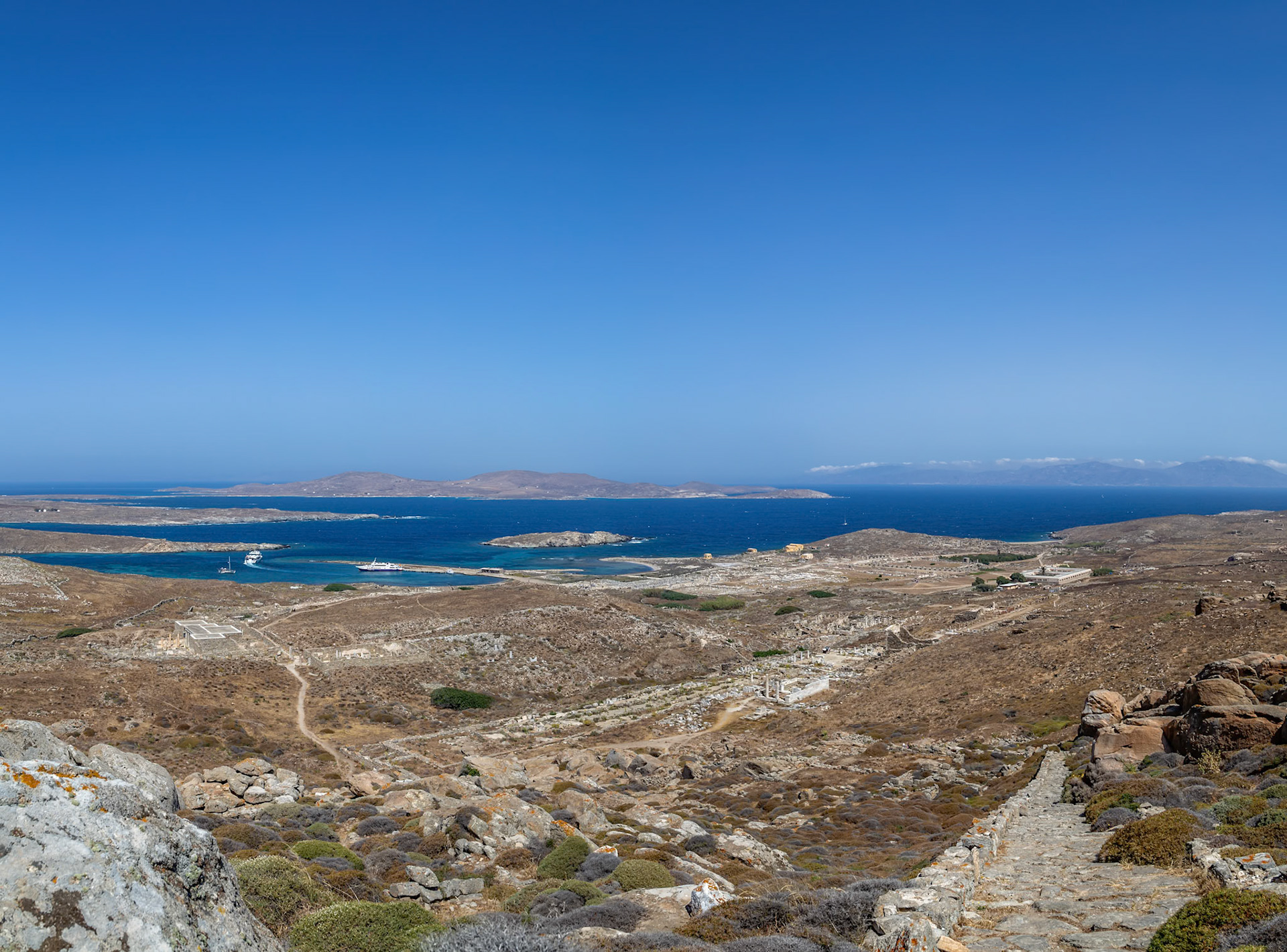 Delos, Greece - May 22nd 2018: A high-angle view shows the ancient ruins of Delos, a Greek island, with the Aegean Sea and other islands in the background.