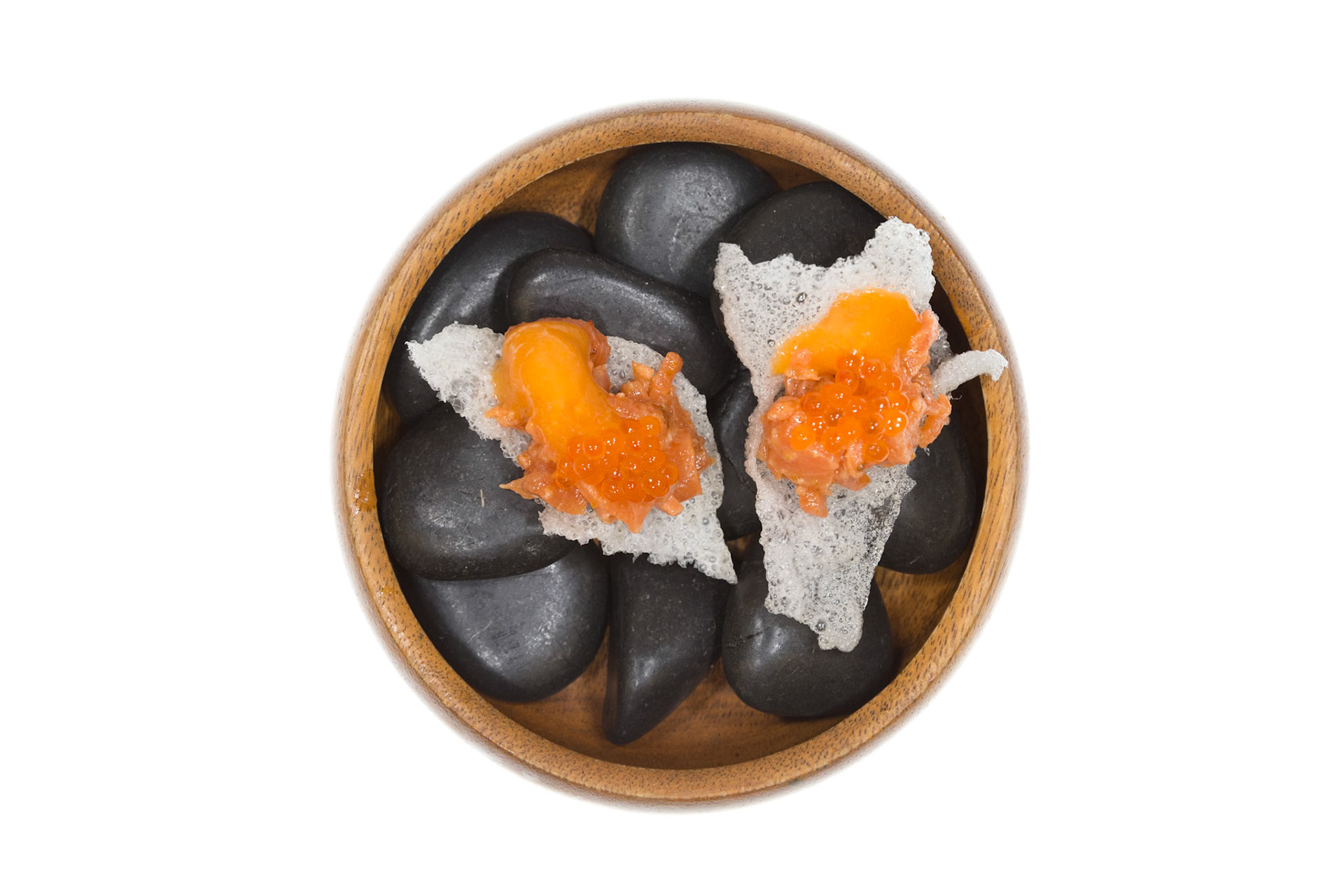 Fog Lark, Portland, Oregon - April 6th 2018: A wooden bowl filled with black rocks and two pieces of food with orange topping.