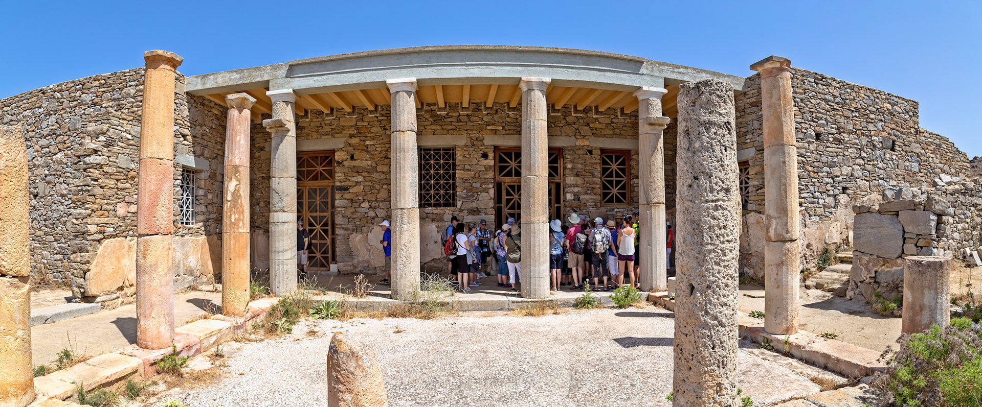 Delos, Greece - May 22nd 2018: A tour group gathers at the entrance of an ancient building with stone walls and columns, exploring the historical site.