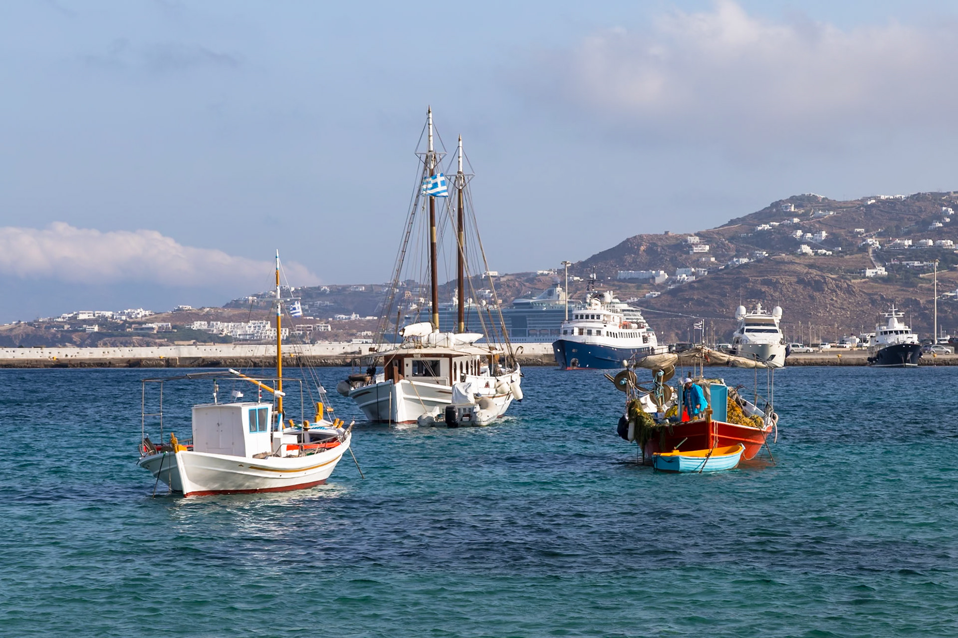 Mykonos, Greece - May 23rd 2018: Fishing boats bob in the Aegean Sea, near the harbor. The Greek flag flies from the mast of the center boat.
