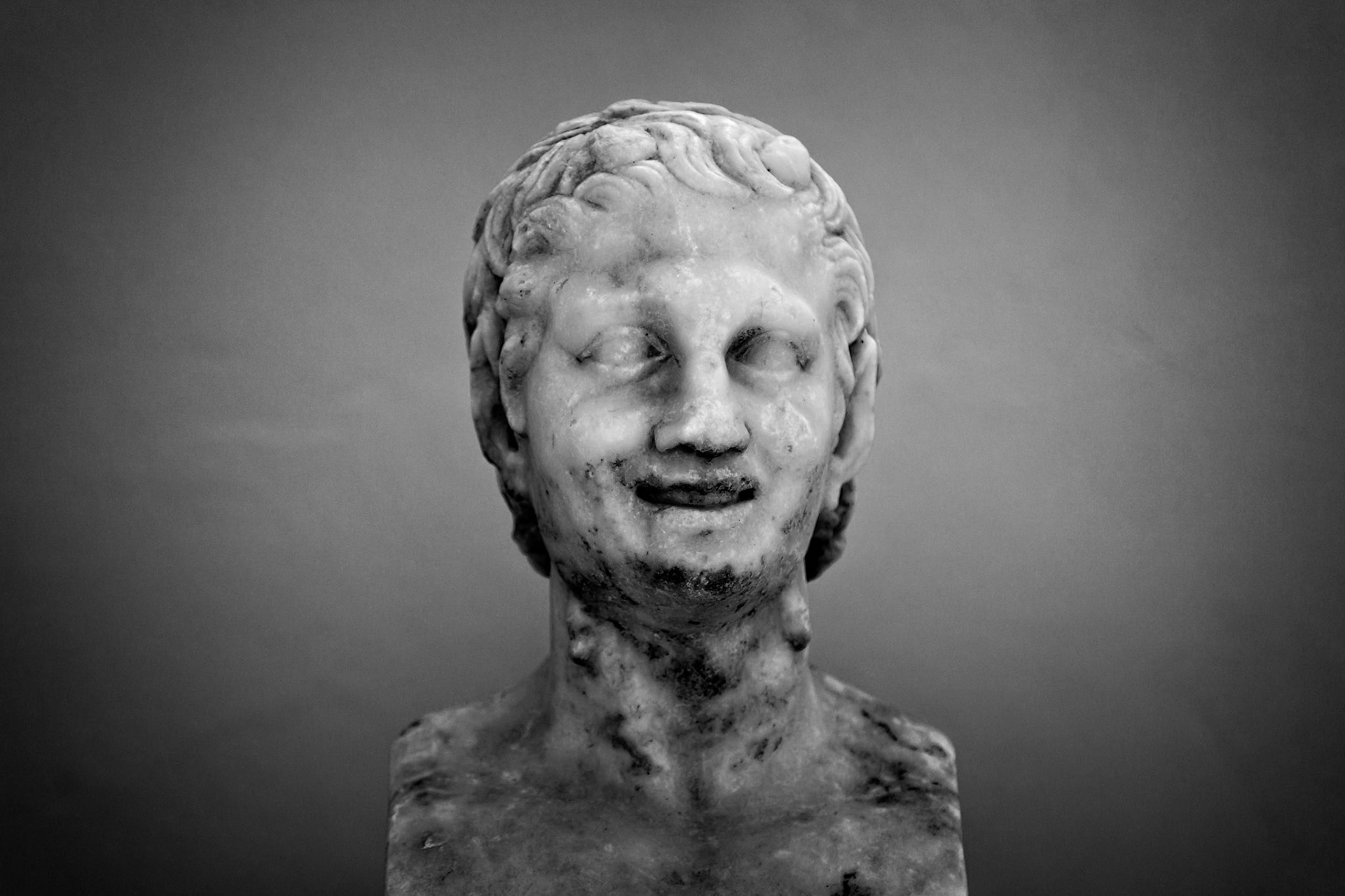 Delos, Greece - May 22nd 2018: A marble bust of a man with a slight smile, likely a depiction of a historical figure or deity, showcasing ancient Greek sculpture.