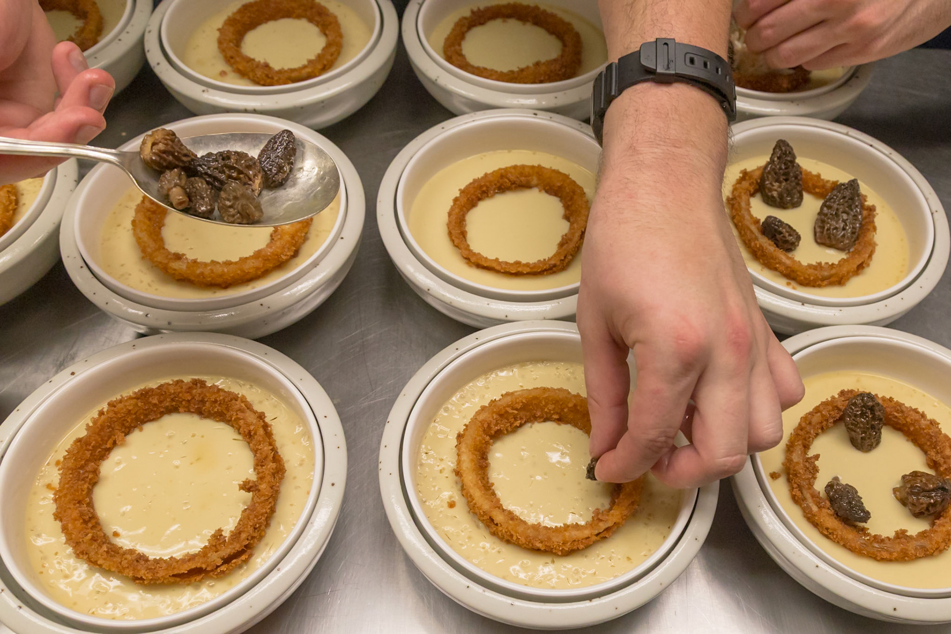 Fog Lark, Portland, Oregon - April 6th 2018: A chef plates a dish with a fried onion ring, sauce, and morel mushrooms, adding the final touches.