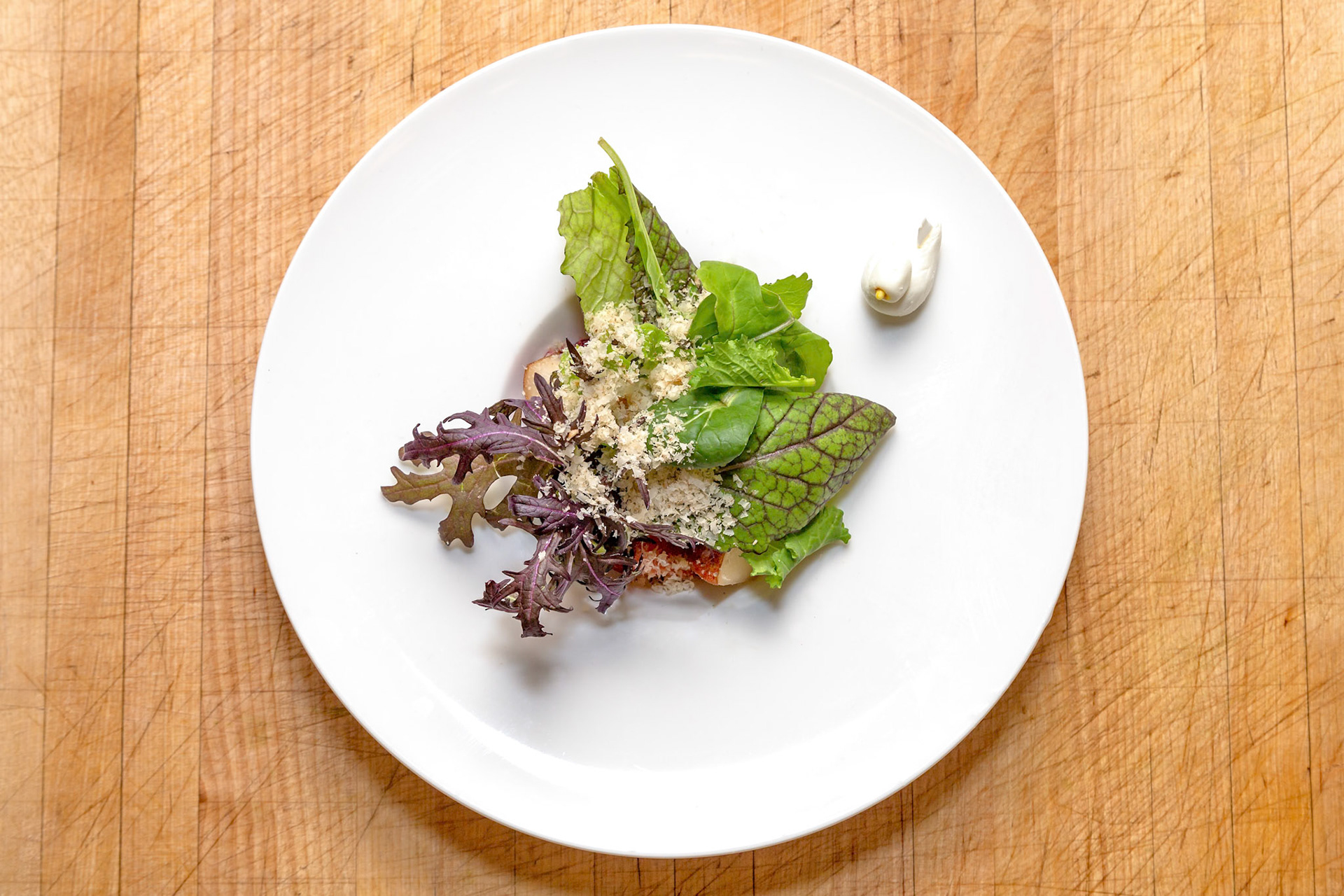 Fog Lark, Portland, Oregon - March 15th 2019: A chef plates a salad with greens, cheese, and a white garnish on a white plate.