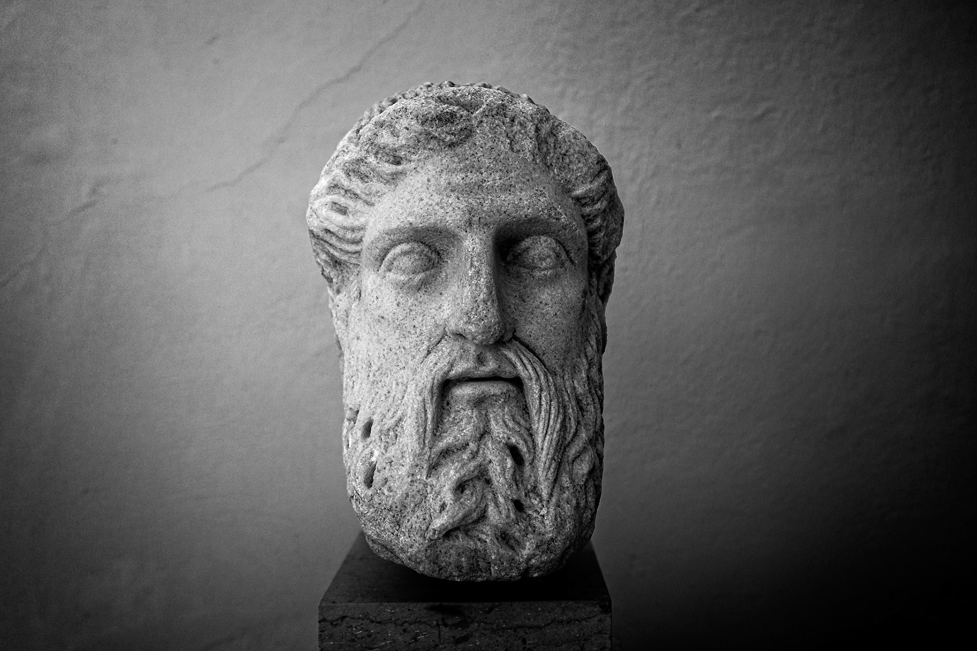 Delos, Greece - May 22nd 2018: A weathered stone head of a bearded man, possibly a deity or philosopher, stands on display, showcasing ancient Greek artistry.