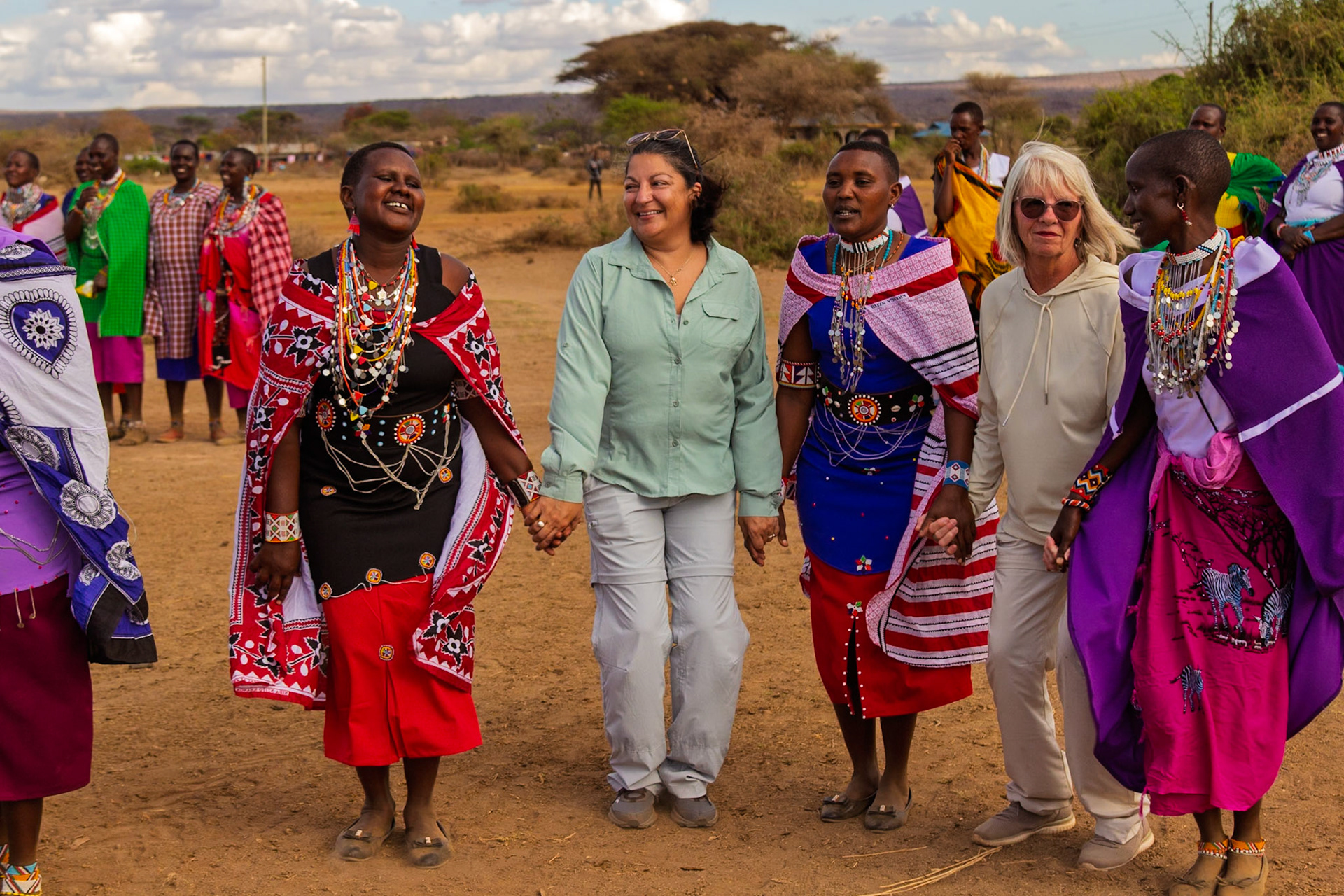 Tourists hold hands with Maasai women in Kenya, sharing a cultural exchange and creating a memorable experience in their village.