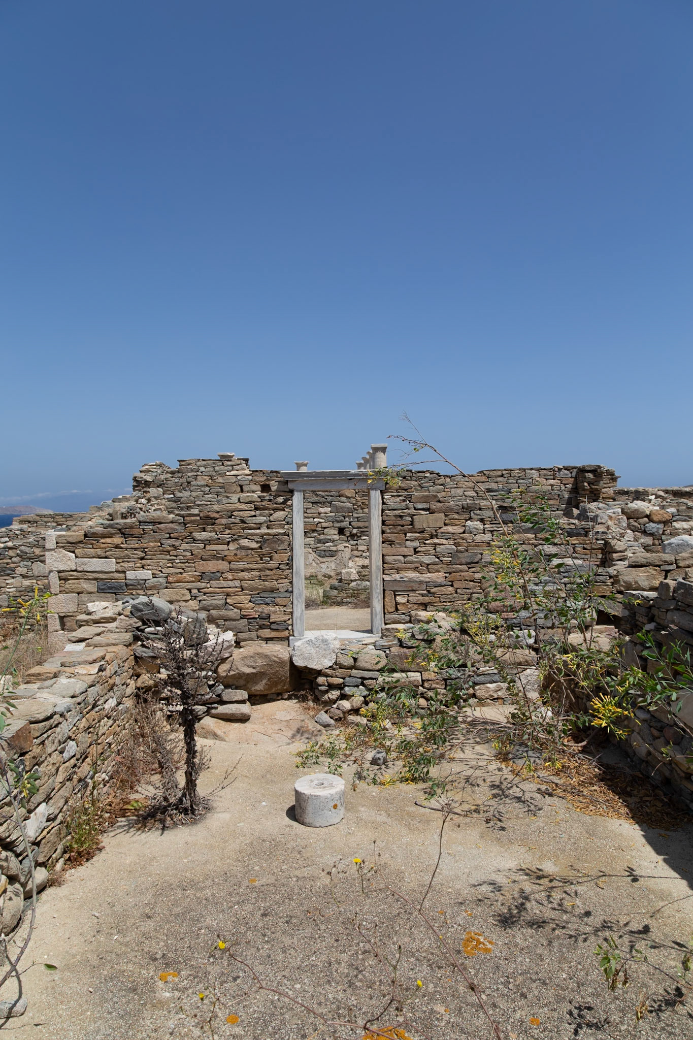 Delos, Greece - May 22nd 2018: Ruins of an ancient building stand against a clear blue sky. The stone walls and doorway offer a glimpse into the past.