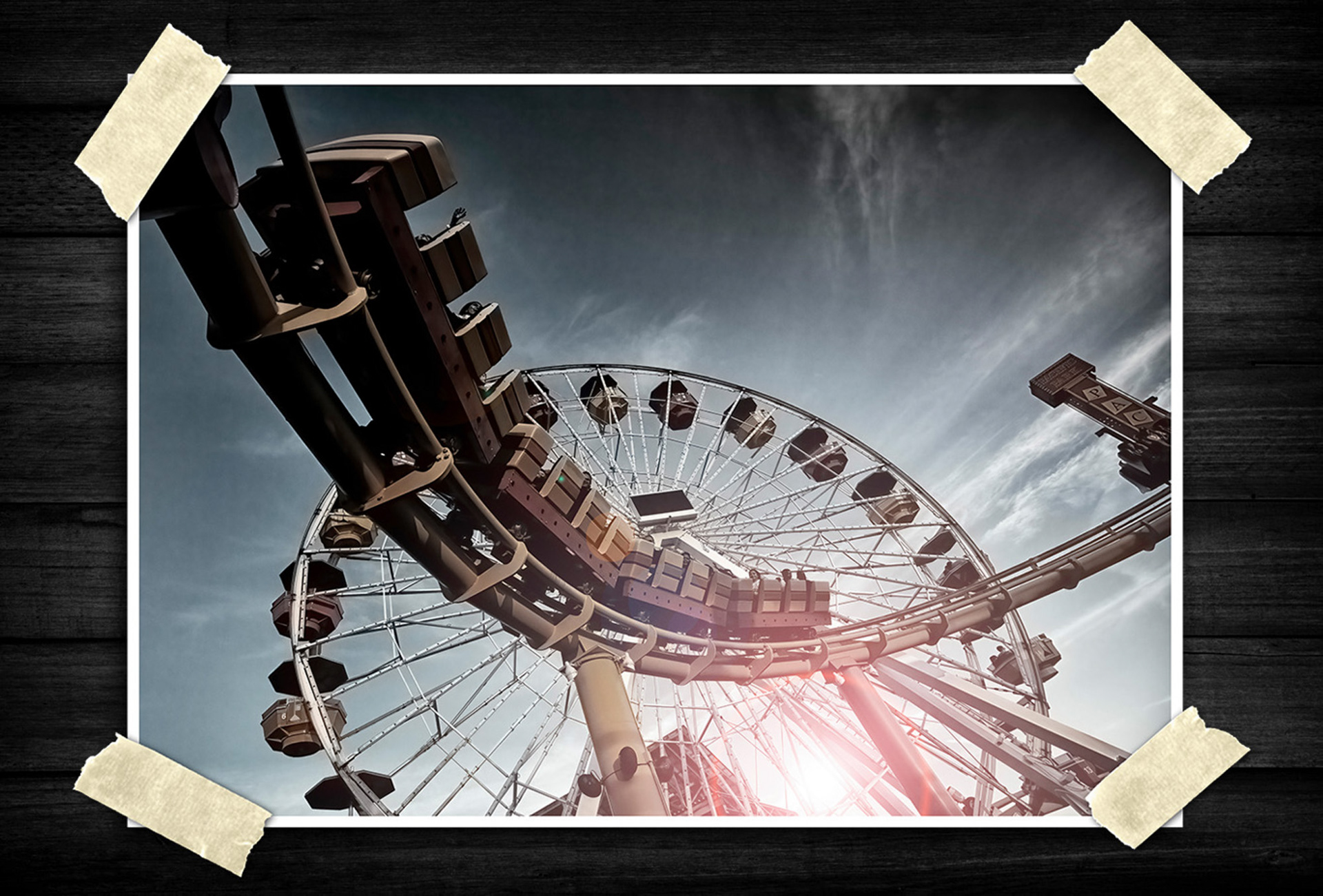 A roller coaster track curves aggressively across the foreground while a large Ferris wheel fills the background. The perspective creates a feeling of speed and motion, even though the image itself is static.