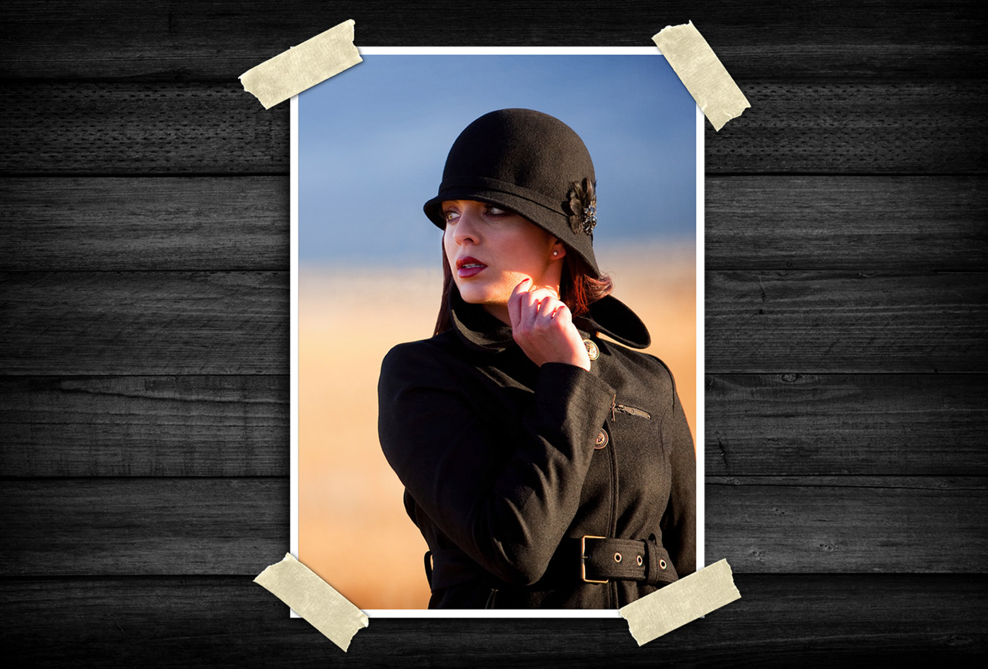 Fashion portrait of a woman wearing a black cloche hat and tailored coat, looking into the distance with warm natural lighting and a softly blurred outdoor background.