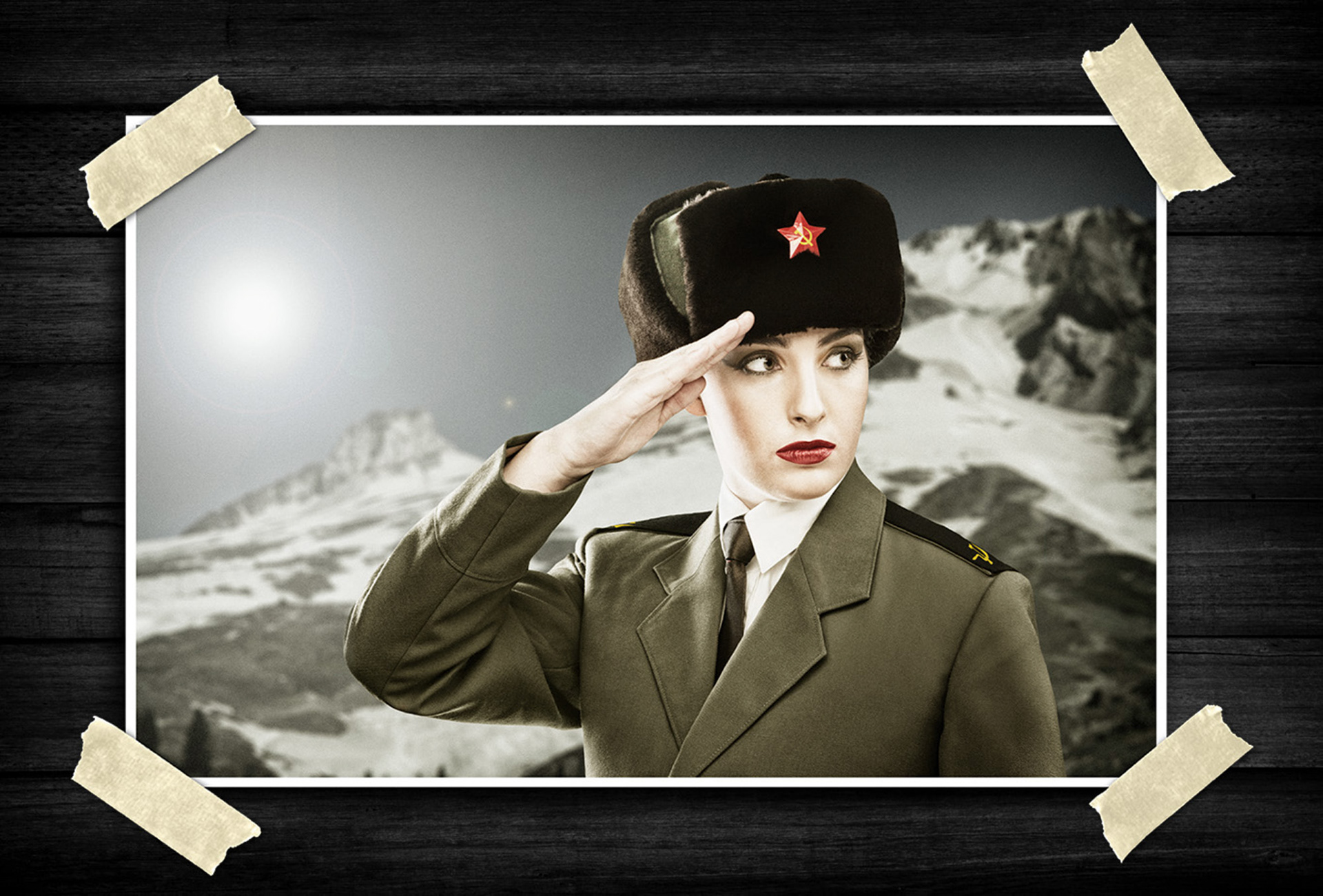 Portrait of a woman in a vintage military-inspired uniform and fur hat, giving a salute against a snowy mountain backdrop in a stylized editorial scene.