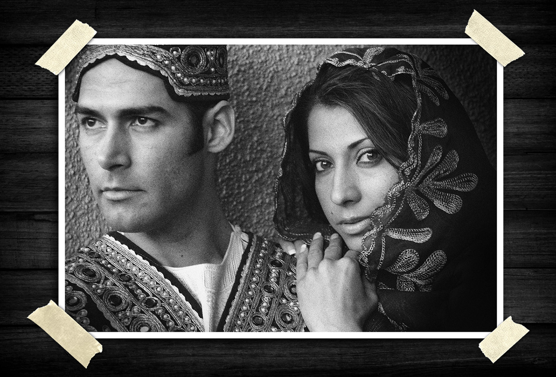 Black-and-white portrait of a man and woman wearing detailed traditional clothing and head coverings, posed side by side with an elegant cultural style.