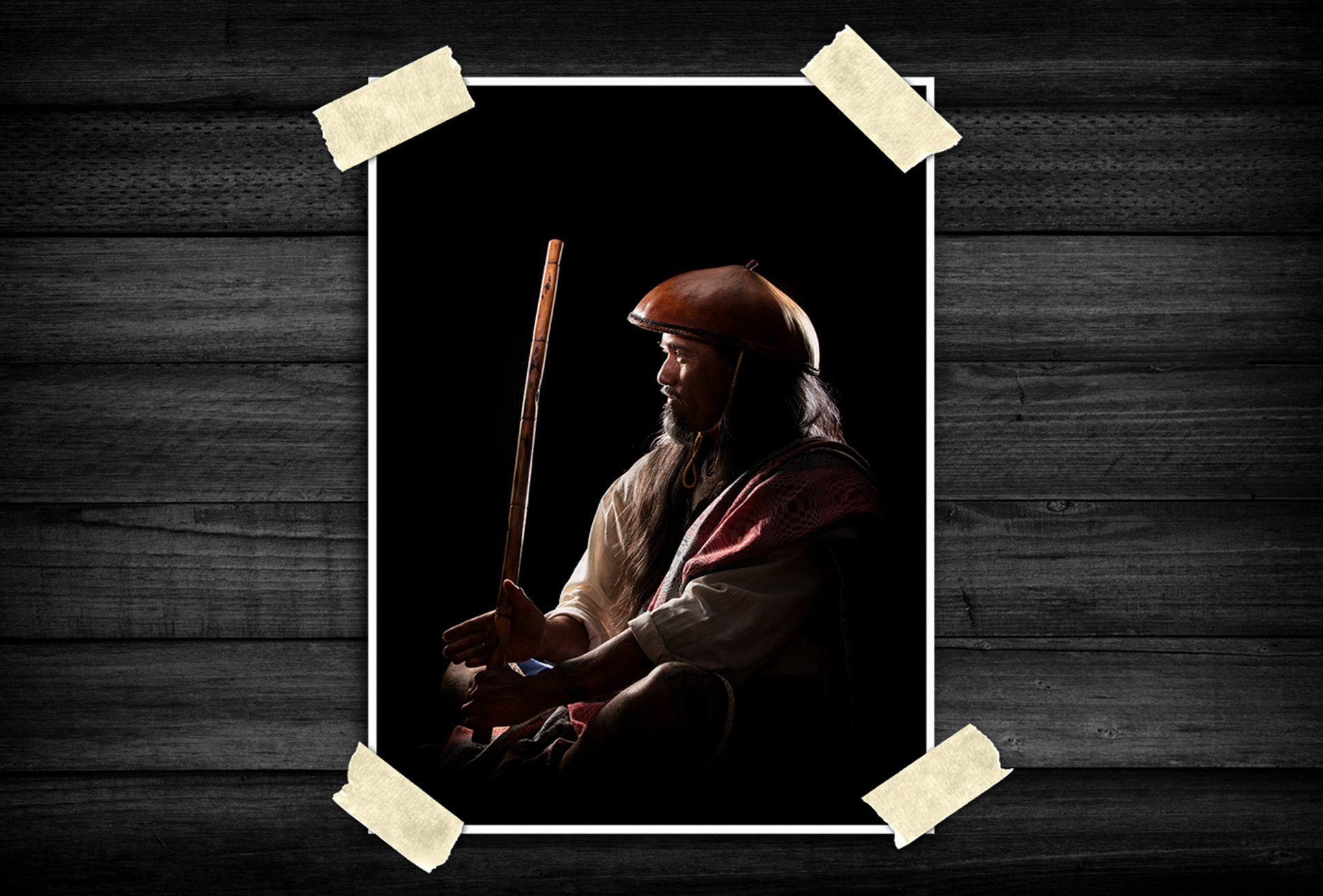 Dramatic studio portrait of a person in traditional attire holding a wooden staff against a dark background with cinematic lighting.