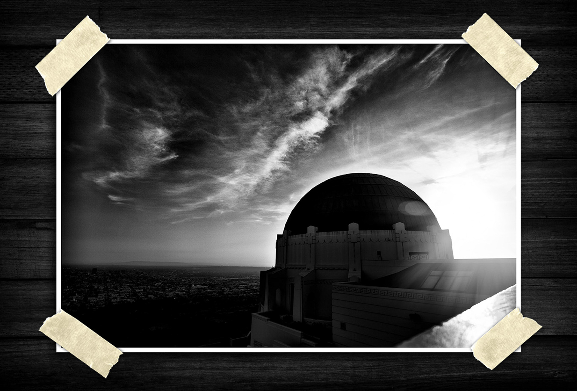 dramatic black-and-white architectural photograph of a large domed observatory building, shot with strong backlighting. The sun is low near the horizon on the right, creating lens flare and deep shadows across the structure. The sky dominates much of the frame with streaking, textured clouds that add a cinematic feel. The composition emphasizes contrast and scale, with the dome standing as the central subject against a vast skyline.