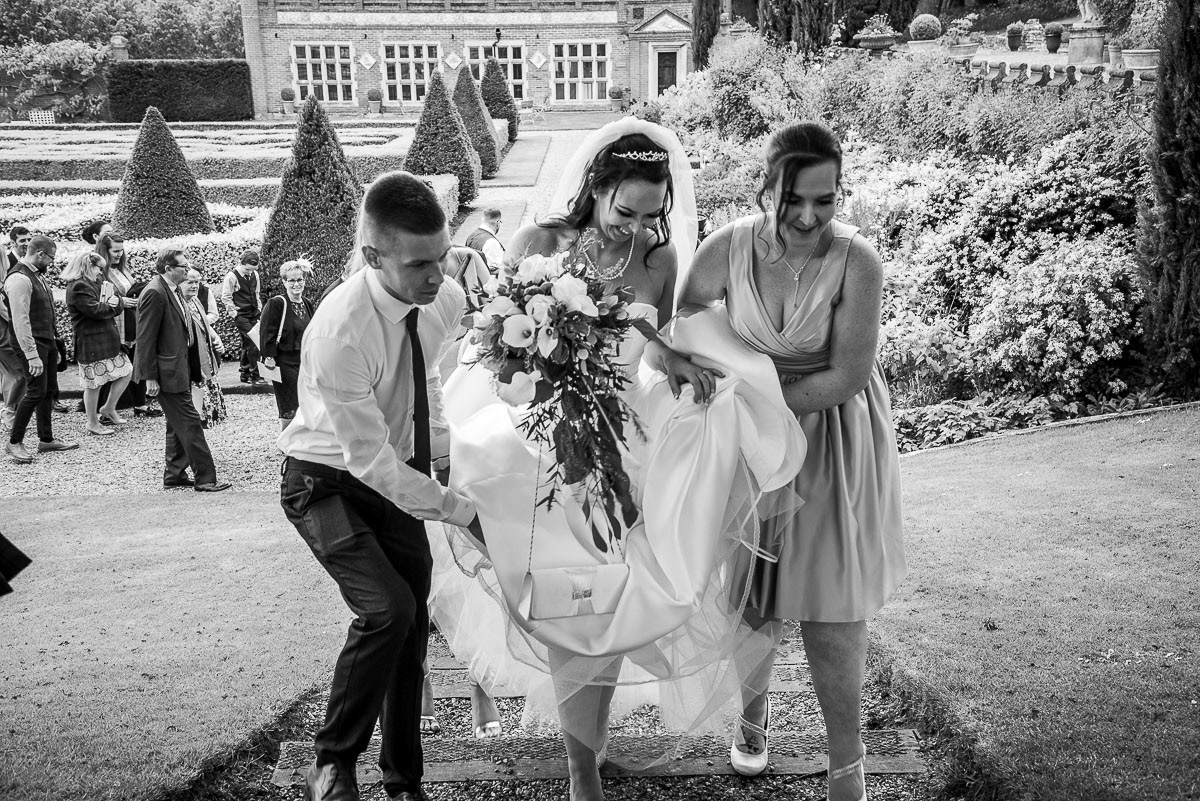 The bride being helped to negotiate the steps in a wedding gown at an Oxnead Hall wedding in Norfolk