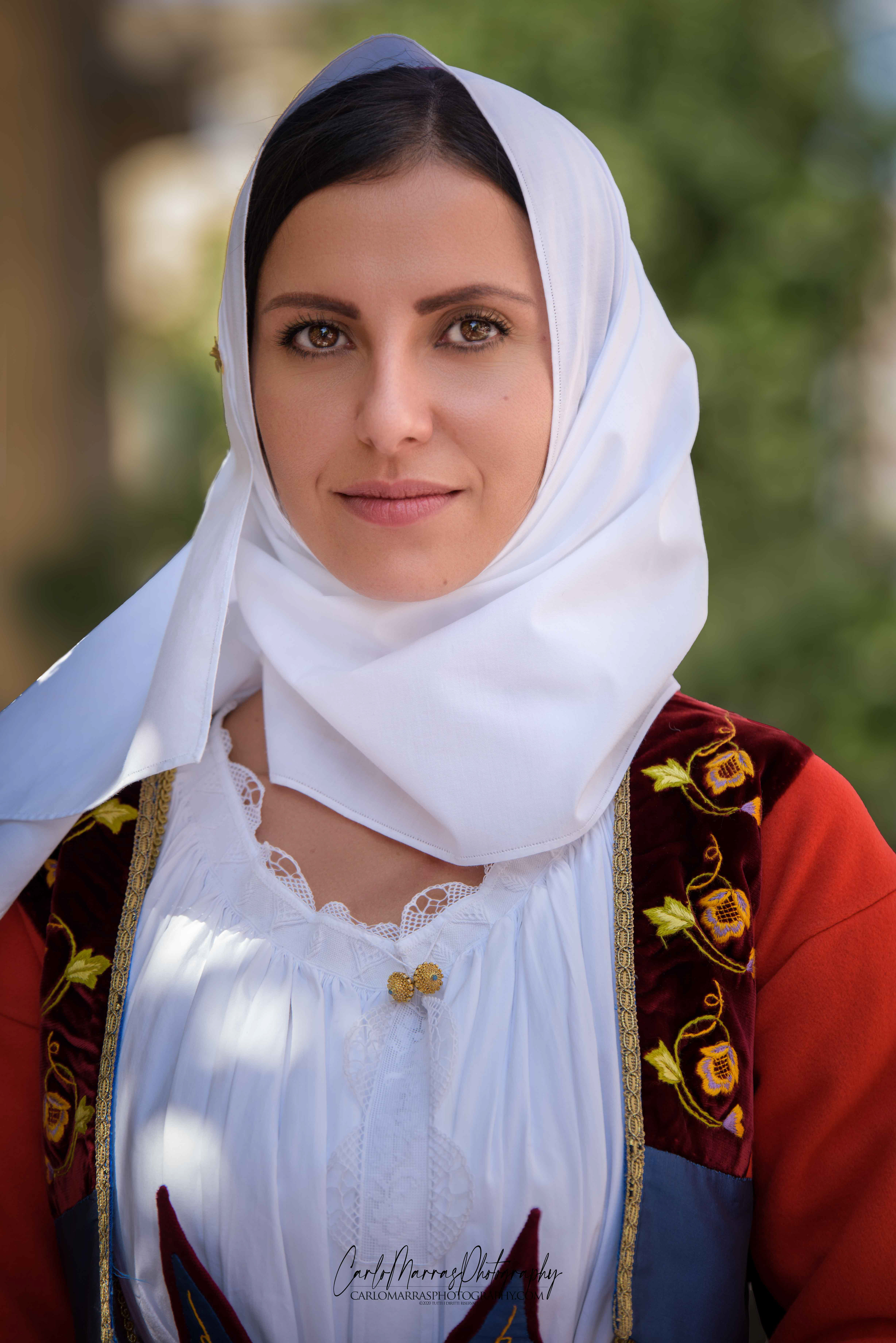 Volti di Sardegna In prima pagina Angela del gruppo folk Brathallos con l’abito tradizionale femminile sardo di Fonni, composto in questa variante da un copricapo di seta o tibet (su mucadore); una camicia bianca chiusa da bottoni in filigrana d’oro (sa amissa); un giacchino in panno o broccato rosso (su cippone); una gonna in panno e orbace rosso (sa amissèdda) indossata sotto un’altra gonna rossa in panno, orbace e seta, decorata e plissettata (sa veste); un coprispalle (sas palas) che diventa una pettorina nella parte anteriore (sas pettòras) e un grembiule a forma triangolare in orbace o panno ornato con ricami di seta (su saùcciu). Variopinto e ricco di decorazioni e ornamenti, il costume sardo di Fonni, paese compreso nella regione storica della Barbagia di Ollolai, in provincia di Nuoro, è sicuramente uno degli abiti tradizionali più riconoscibili dell’isola. Con i suoi colori accesi e i motivi floreali ricamati nelle stoffe accuratamente lavorate, è possibile ammirarne la bellezza in occasione delle manifestazioni folkloristiche del paese oltre che durante le molteplici feste e sagre della Sardegna. Puoi scoprire tante altri miei scatti nella sezione "folk" e nella nuova rubrica "Volti di Sardegna". (ultimo aggiornamento dicembre 2020)