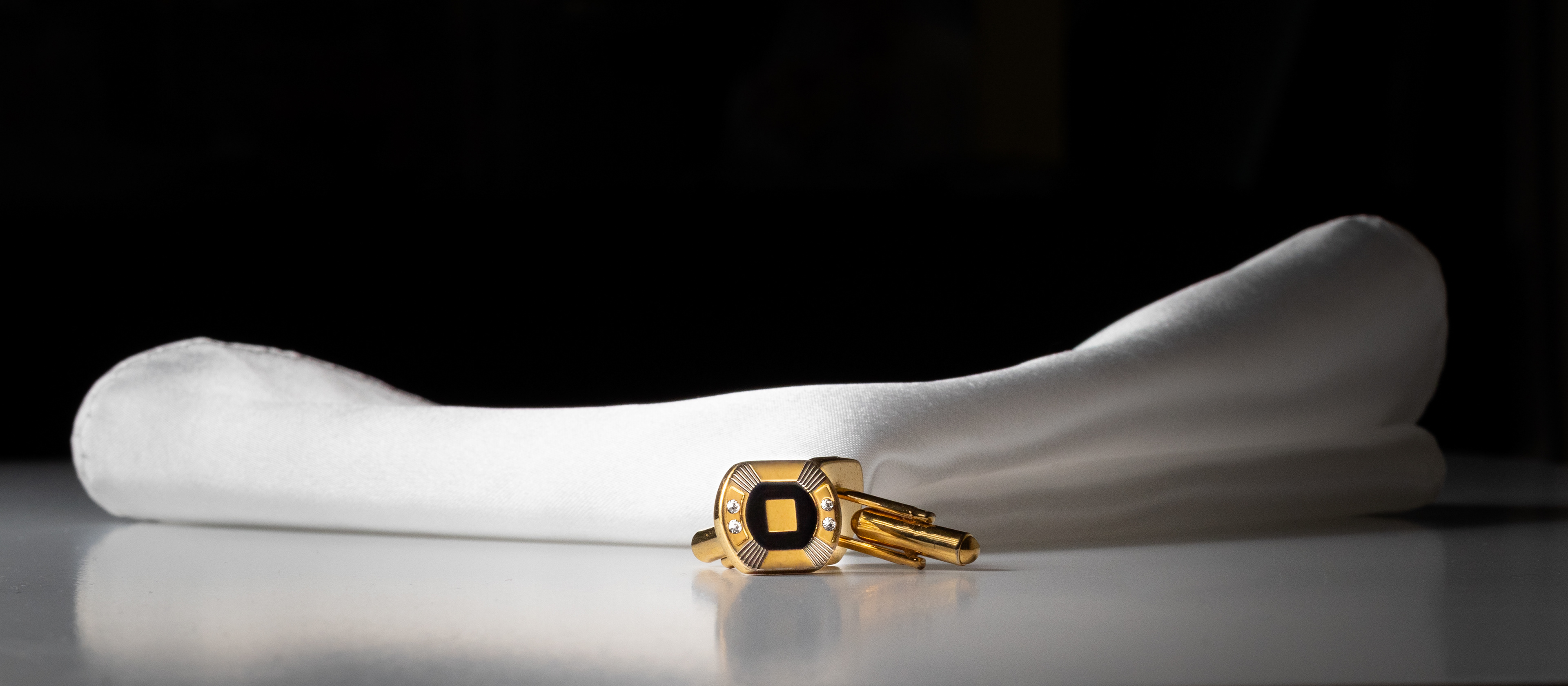 gold cufflinks with diamonds on white surface with white handkerchief 
