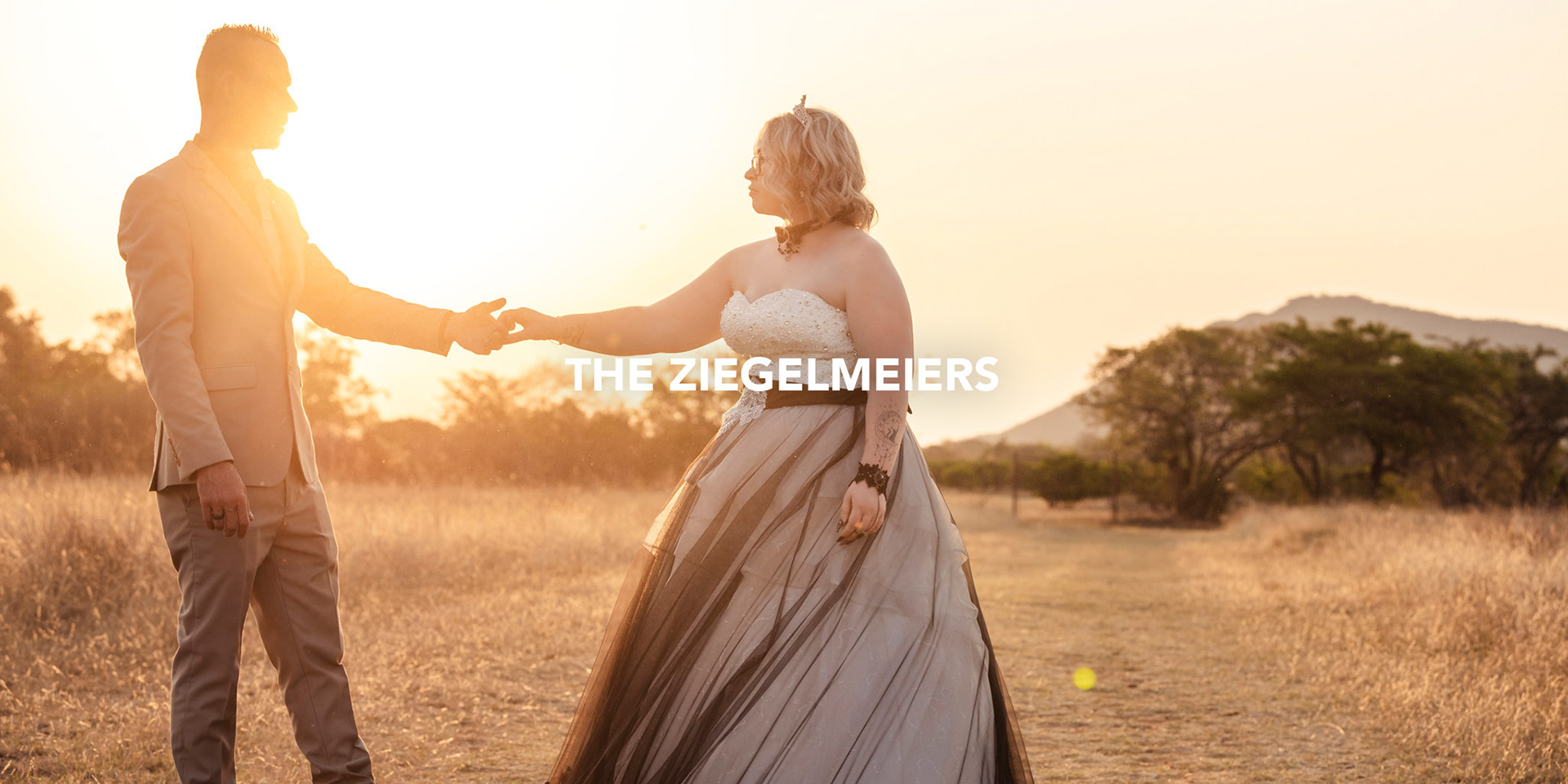 wedding couple bride and groom standing in a field hand in hand dancing at sunset in the south african bush with a mountain in the background photographed by black rock studio