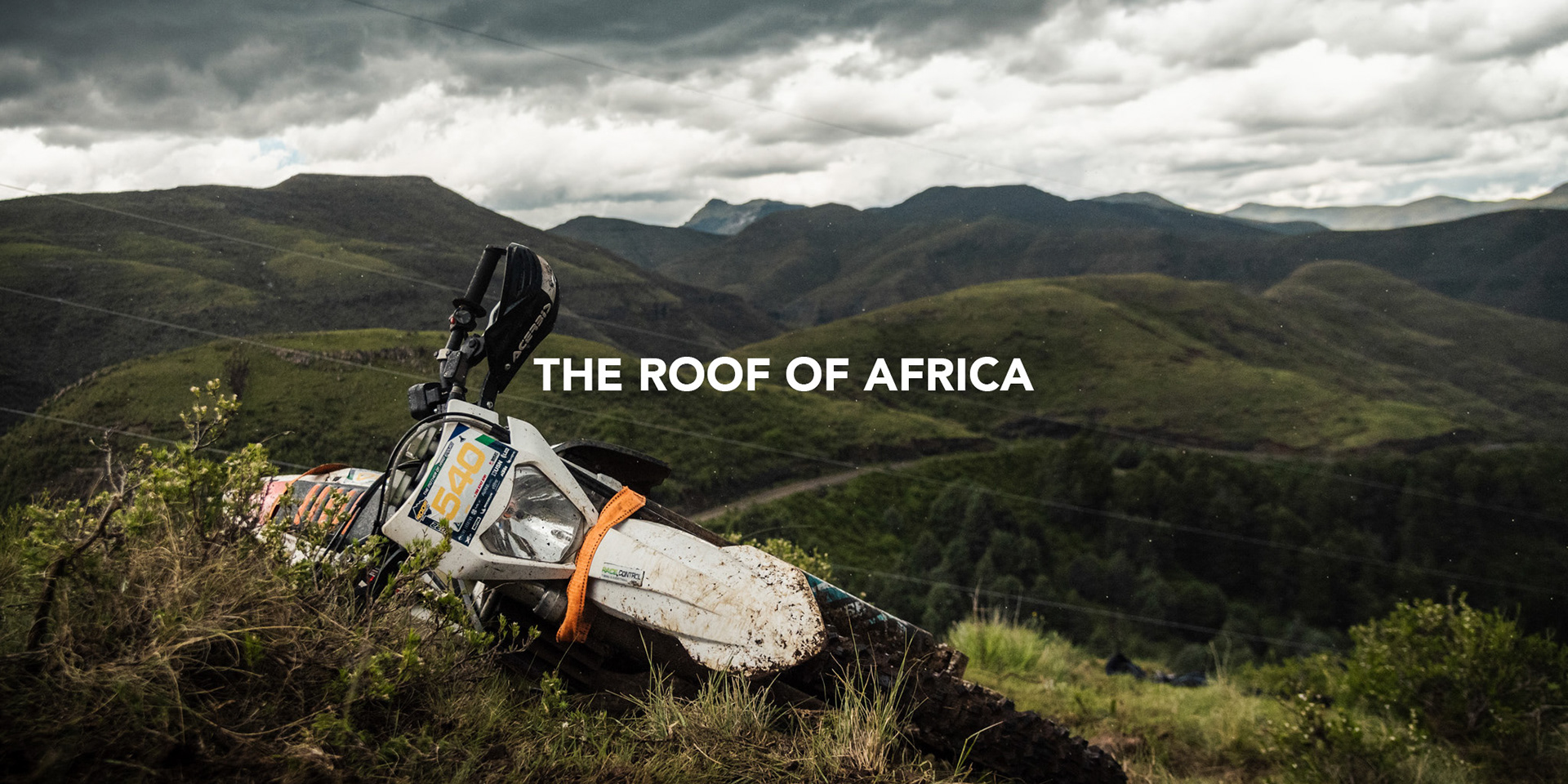 husqvarna enduro motorcycle lying on the side of a mountain in lesotho with a dramatic cloudy backdrop and rain droplets falling during the roof of africa hard enduro photographed by black rock studio