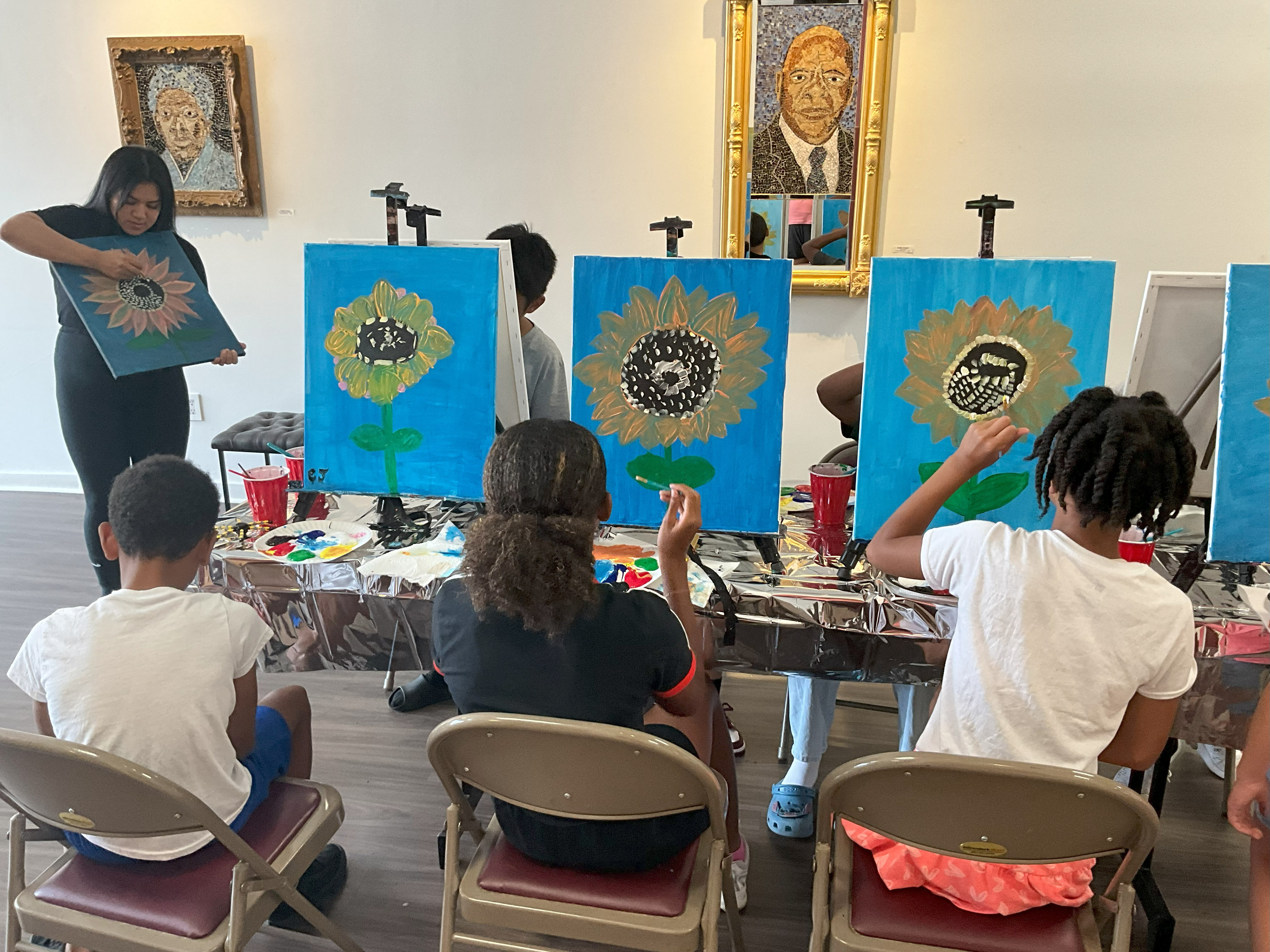 The art teacher is teaching kids how to paint their paintings of sunflowers.