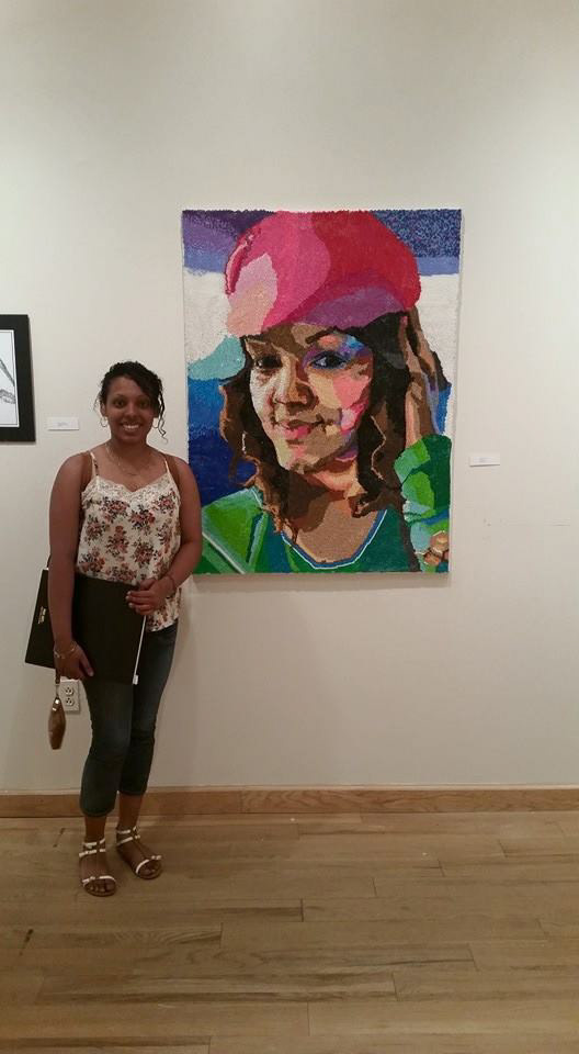 Sasha Cubero standing in front of a bead-type portrait at a student art exhibition