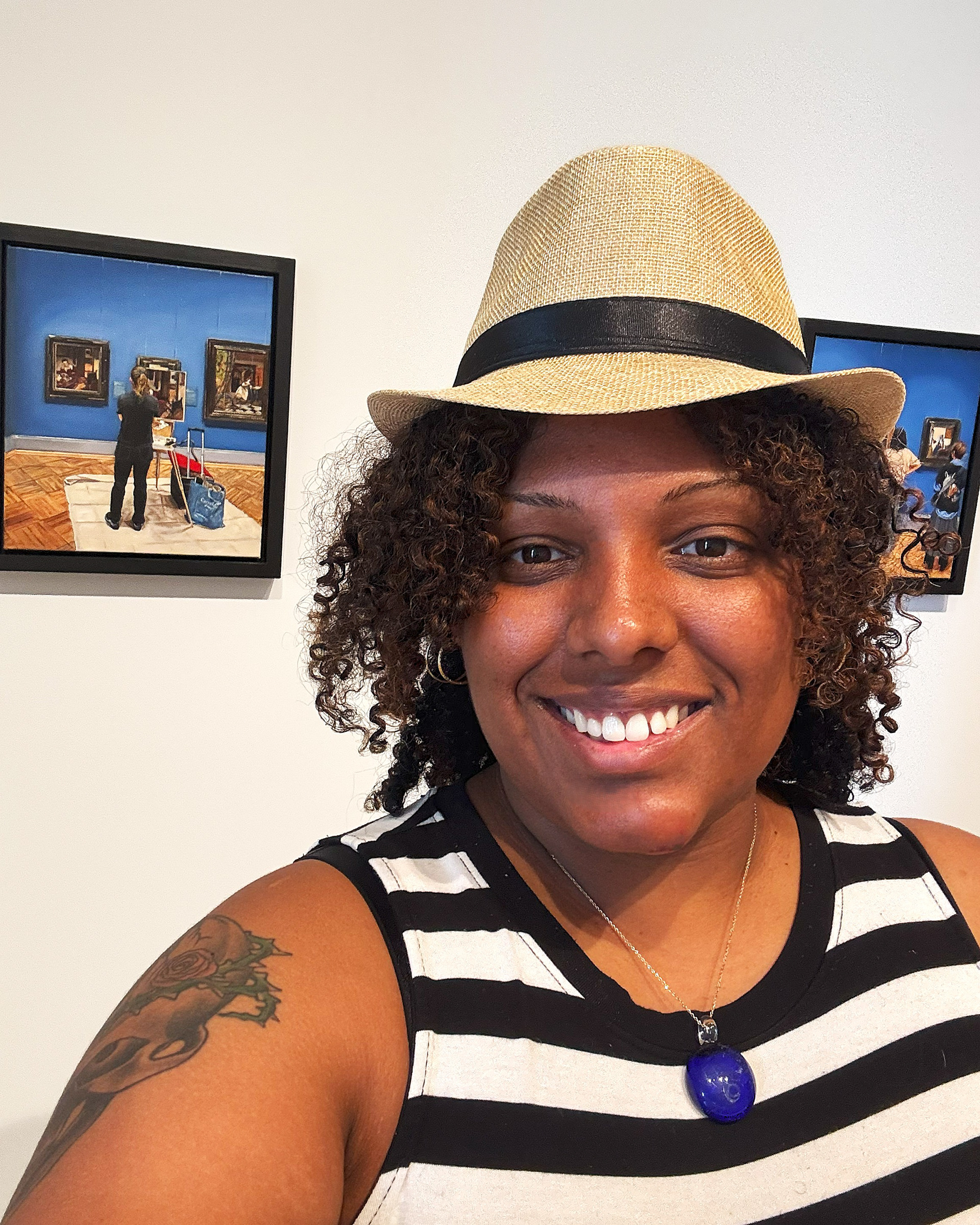 This shows a selfie picture of Sasha Cubero in front of some Joe Fig's paintings.