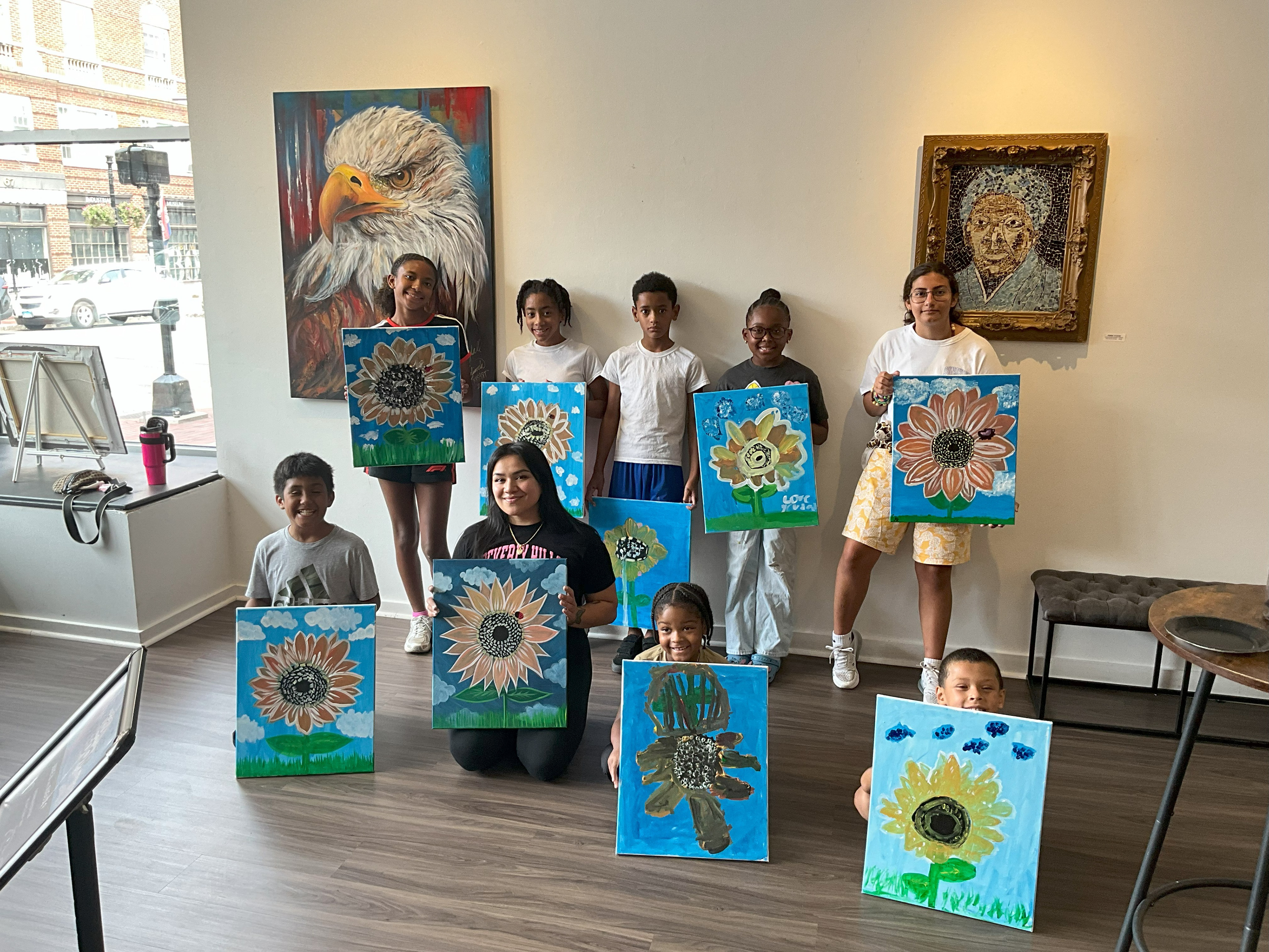 The artist and the kids are posing for a picture with their paintings.