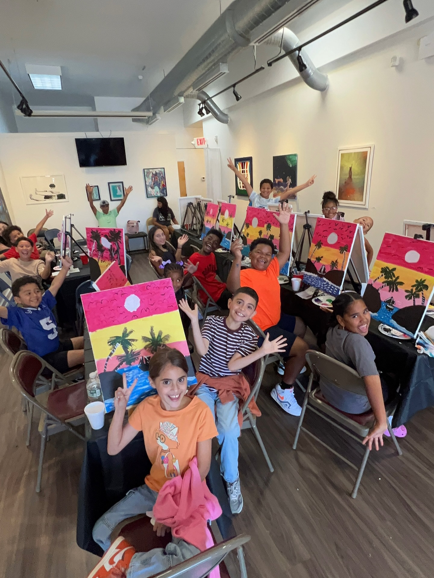 Students in Fiyabomb's class posing for picture while sitting in front of their paintings.