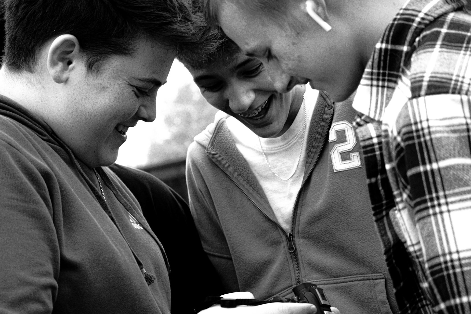 Digital Photography students Hunter Creguer, Aidan Cousineau, and Gavin VanderHoff share a laugh while checking their photos outside the South Art Studio.(Photo by Owen Rounds)