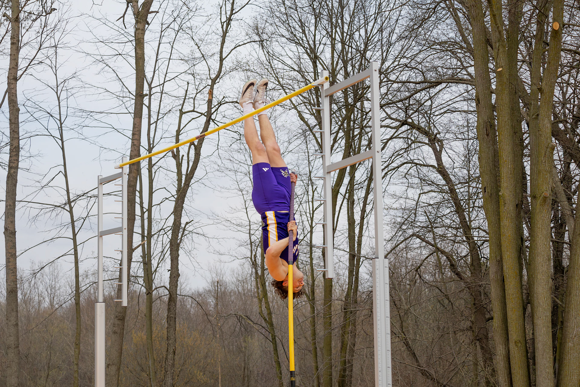 Senior Ben Moss hangs upside down in perfect line with the pole as he prepares for his landing, showing control and precision during his vault. (Photo by Addie Visel)
