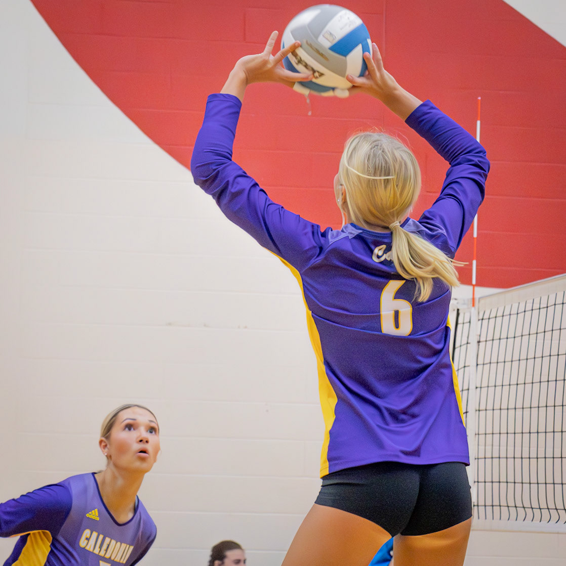 Jumping for the ball, Reese Stafford gives Kyla Charles a perfect set for her to spike over the net. (Photo by Ella Grace Wickens)