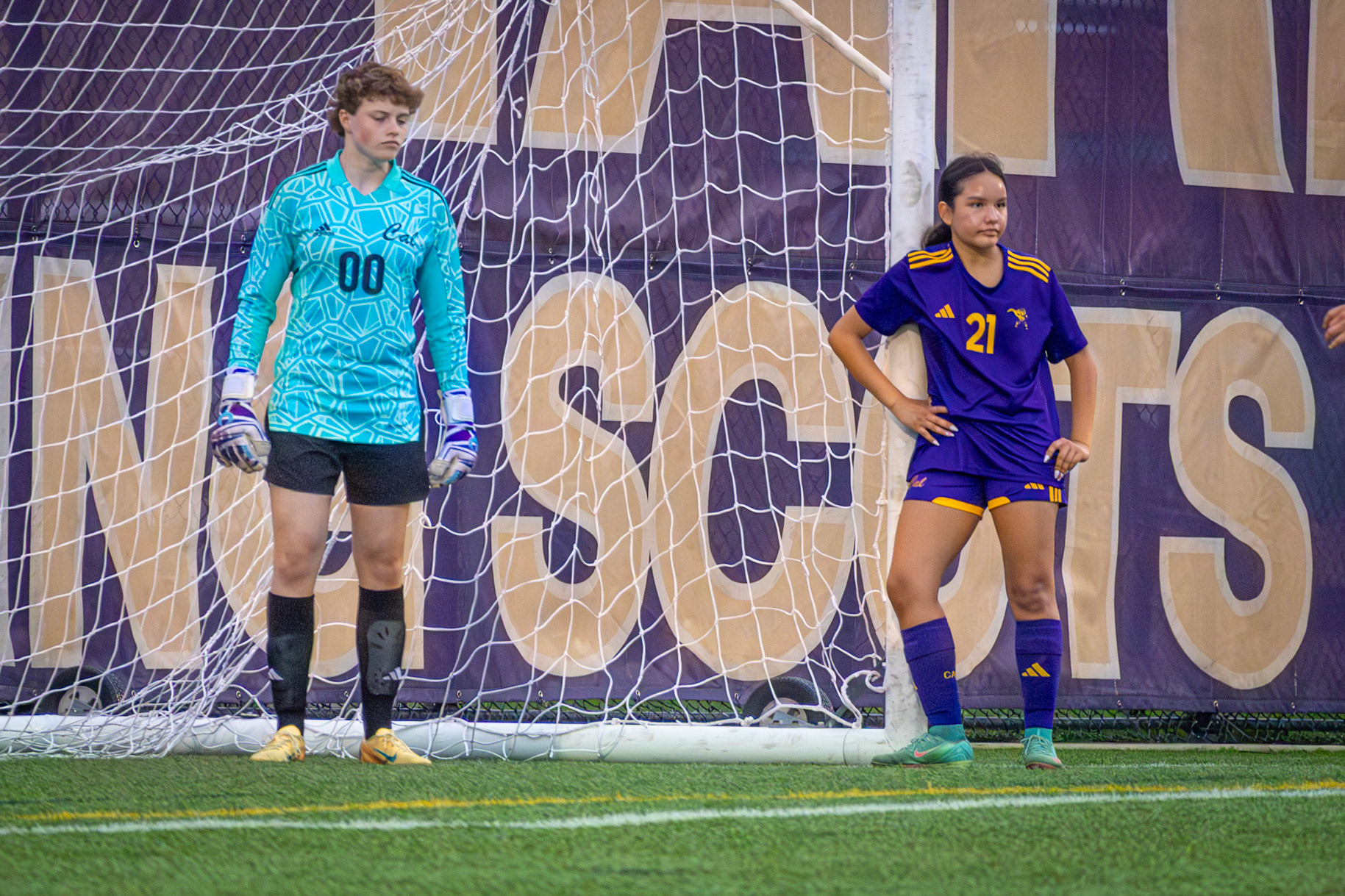 Lilli Ward and Jazmyn Thompson lean against the goalpost, waiting as their team wraps up warmups before the game begins. (Photo by Ava LaBine)
