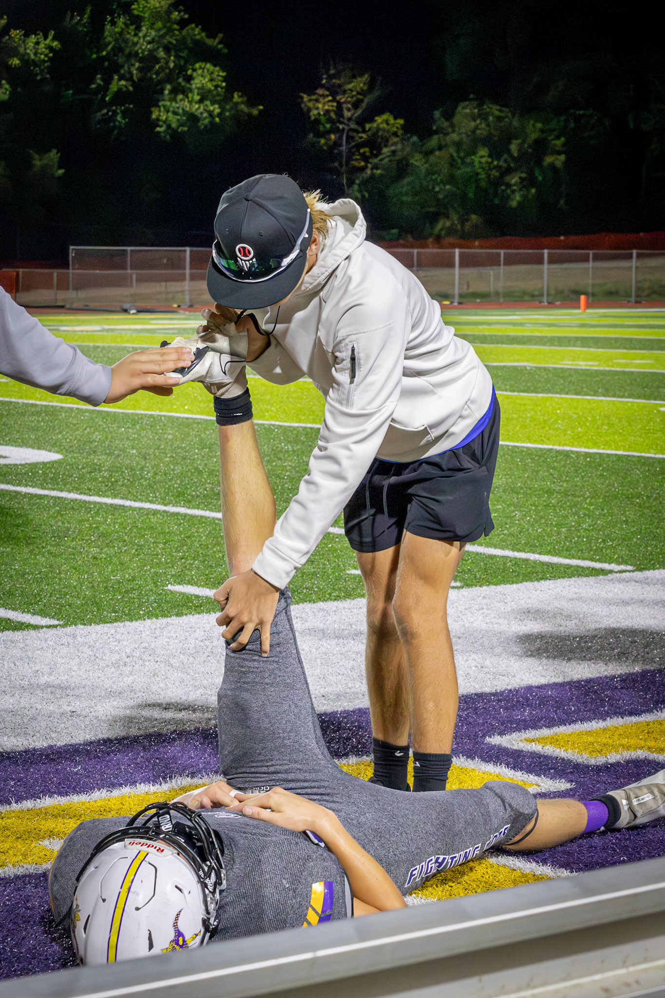 Alexander Spinney stretches Evan Crater's leg so he can be ready to run the next play. (Photo by Sydney Palmer)