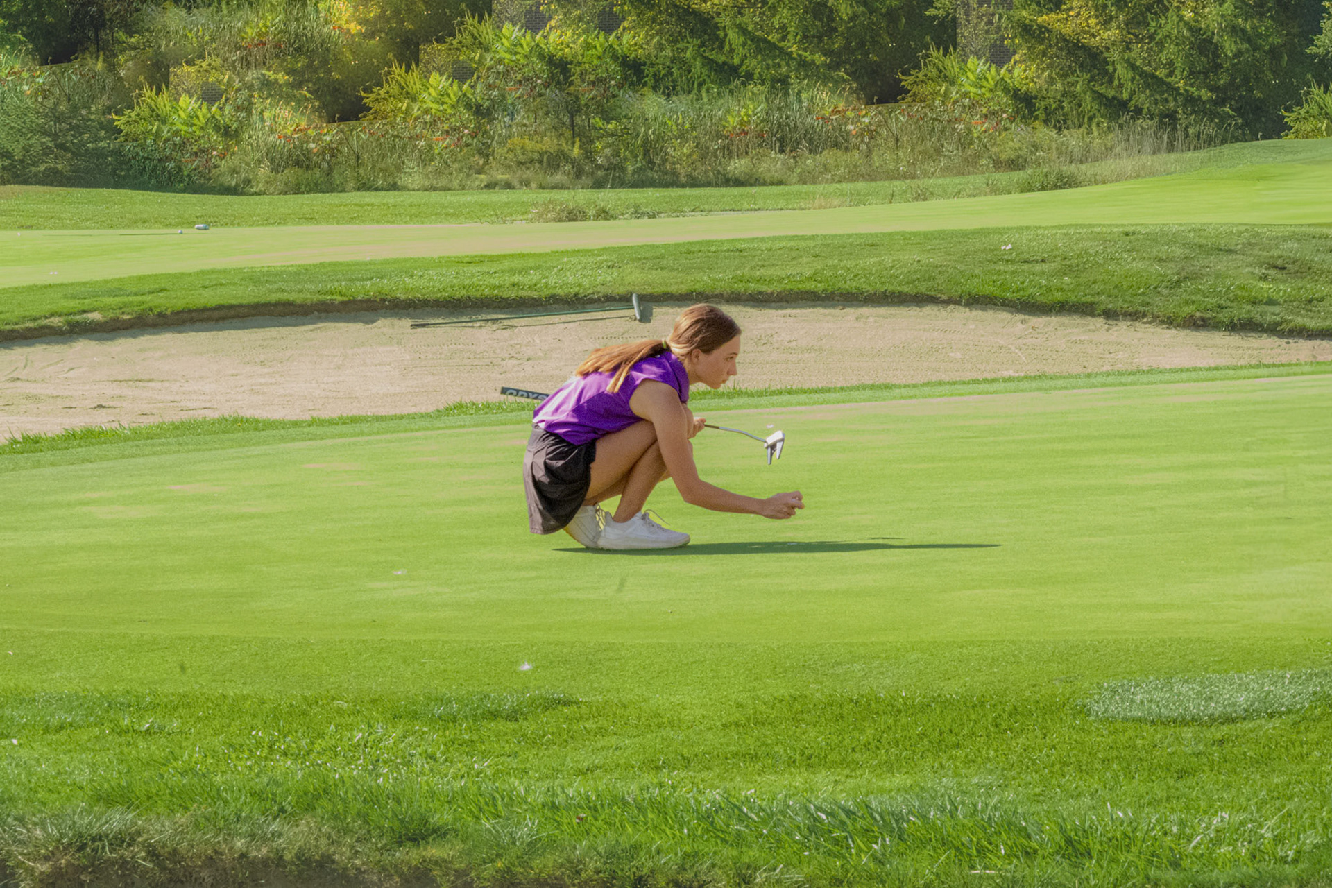 Junior Lauren Scheid kneels down to read the line on her putt. (Photo by Ryder Born)