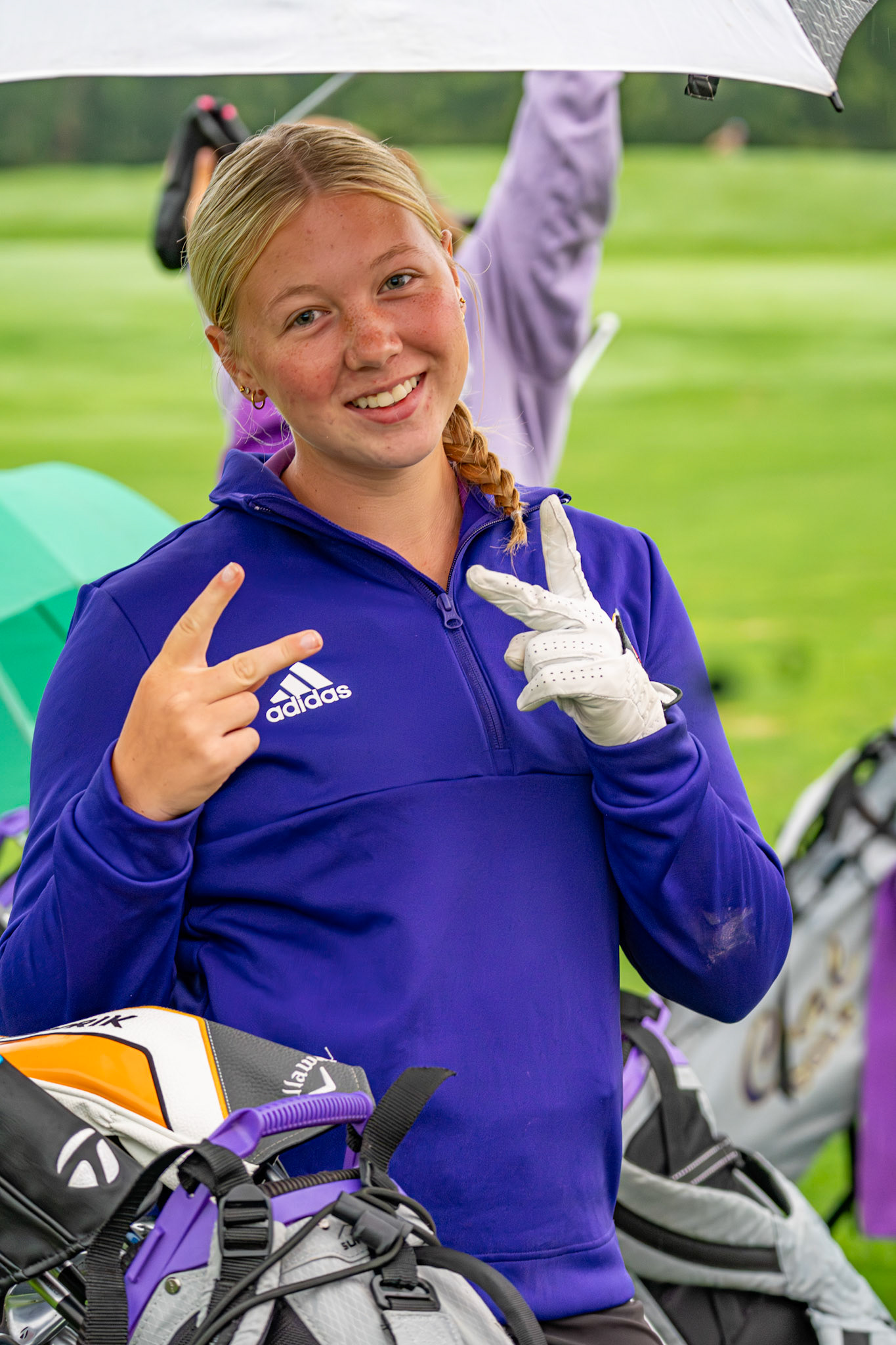 Emily Walbeck flashes musters a smile under an umbrella on a rainy day at the golf course. (Photo by Jolie King)