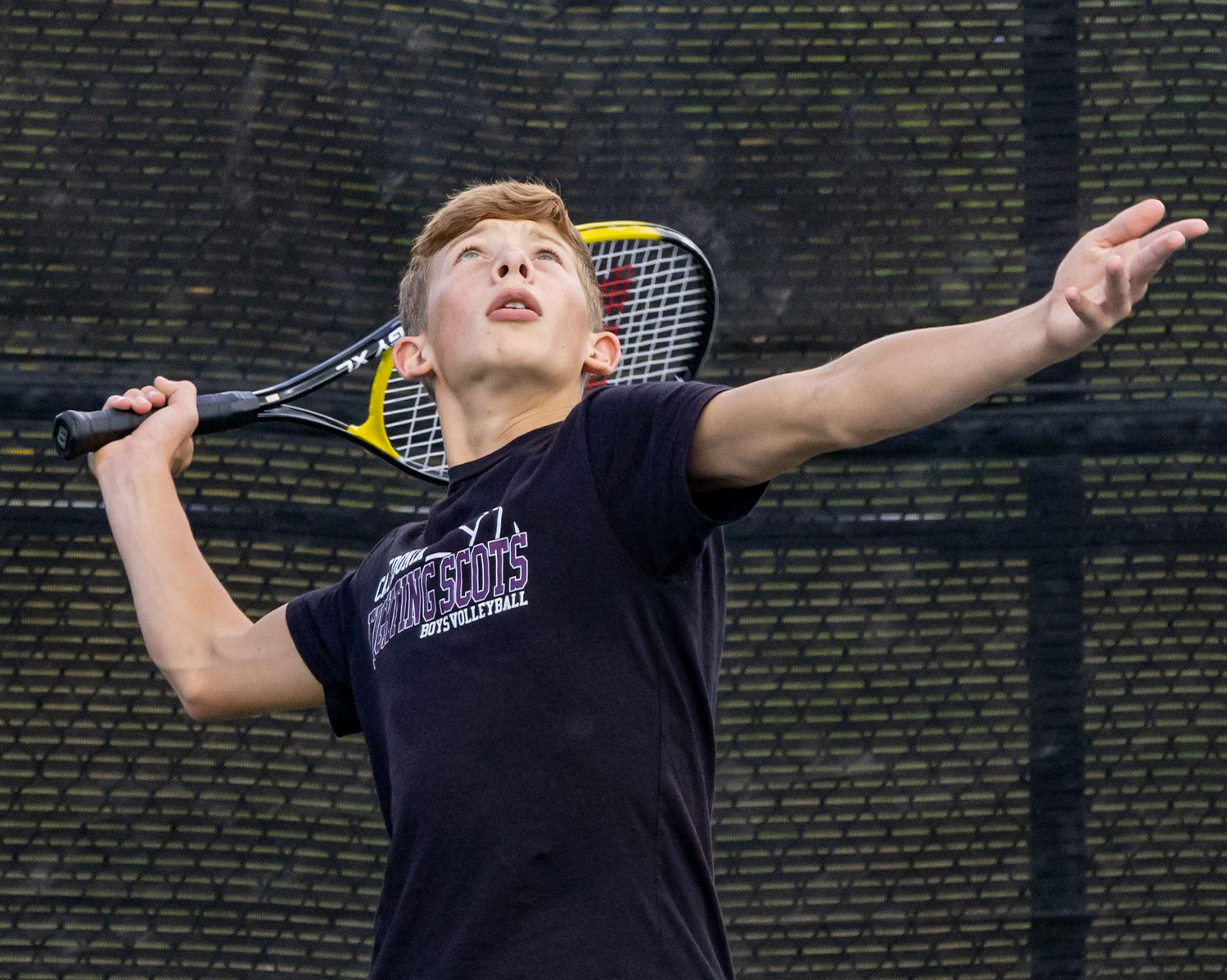 Eli Hanna tosses the ball and pulls back his arm to hit it diagonally across the court.(Photo by Ella-Grace Wickens)