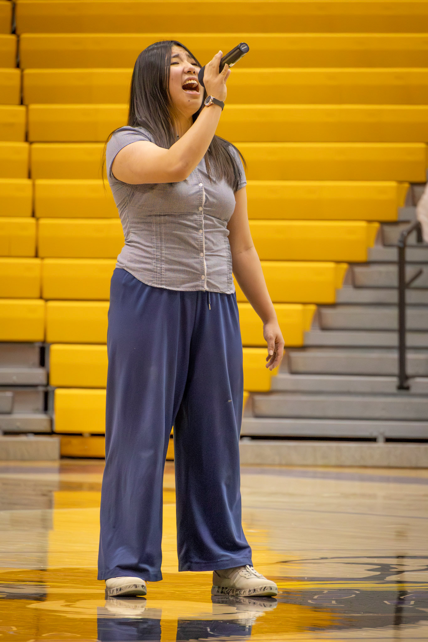 As the crowd rises, Made Mai takes center court, her heartfelt performance of the national anthem uniting the gym before the varsity showdown begins. (Photo by Mackenzie Popma)