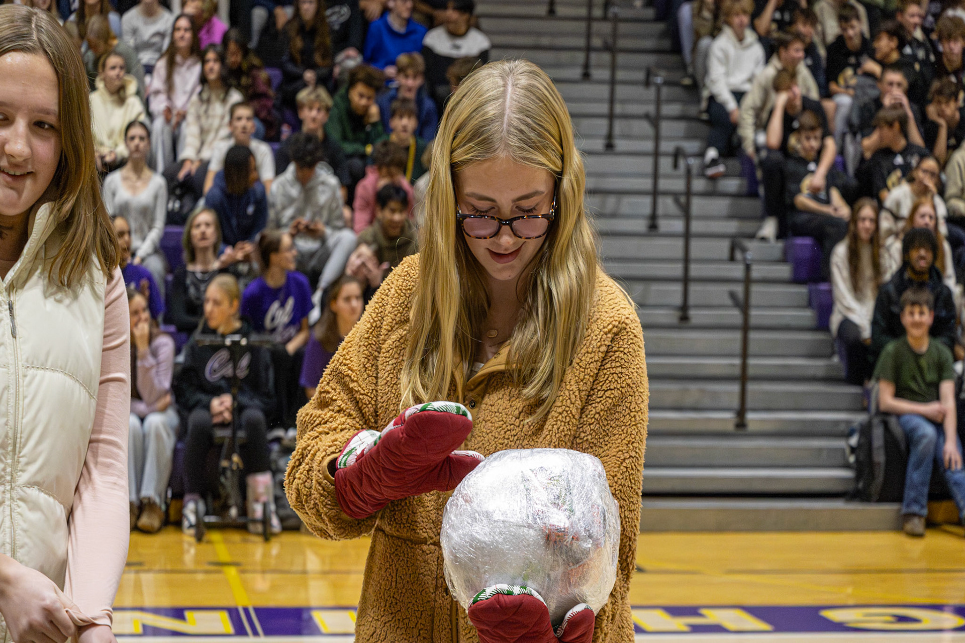 Working to unwrap a tight ball of plastic wrap while also wearing oven mits, Emma Petz hurries to win the candy and prizes inside. (Photo by Ella-Grace Wickens)