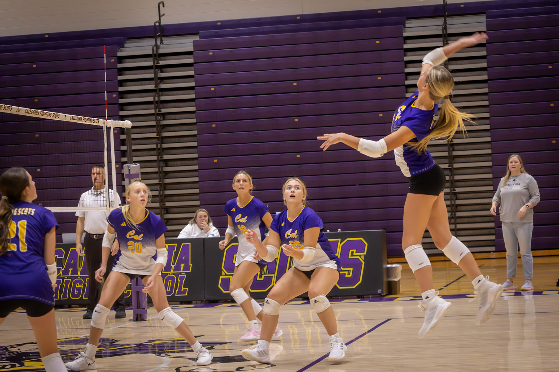 TIMING Brooke Haynes explodes off the floor for a powerful spike, perfectly timed above the net. Her teammates watch intently from their ready positions, prepared for whatever comes next. (Photo by Aslyn Crocker)