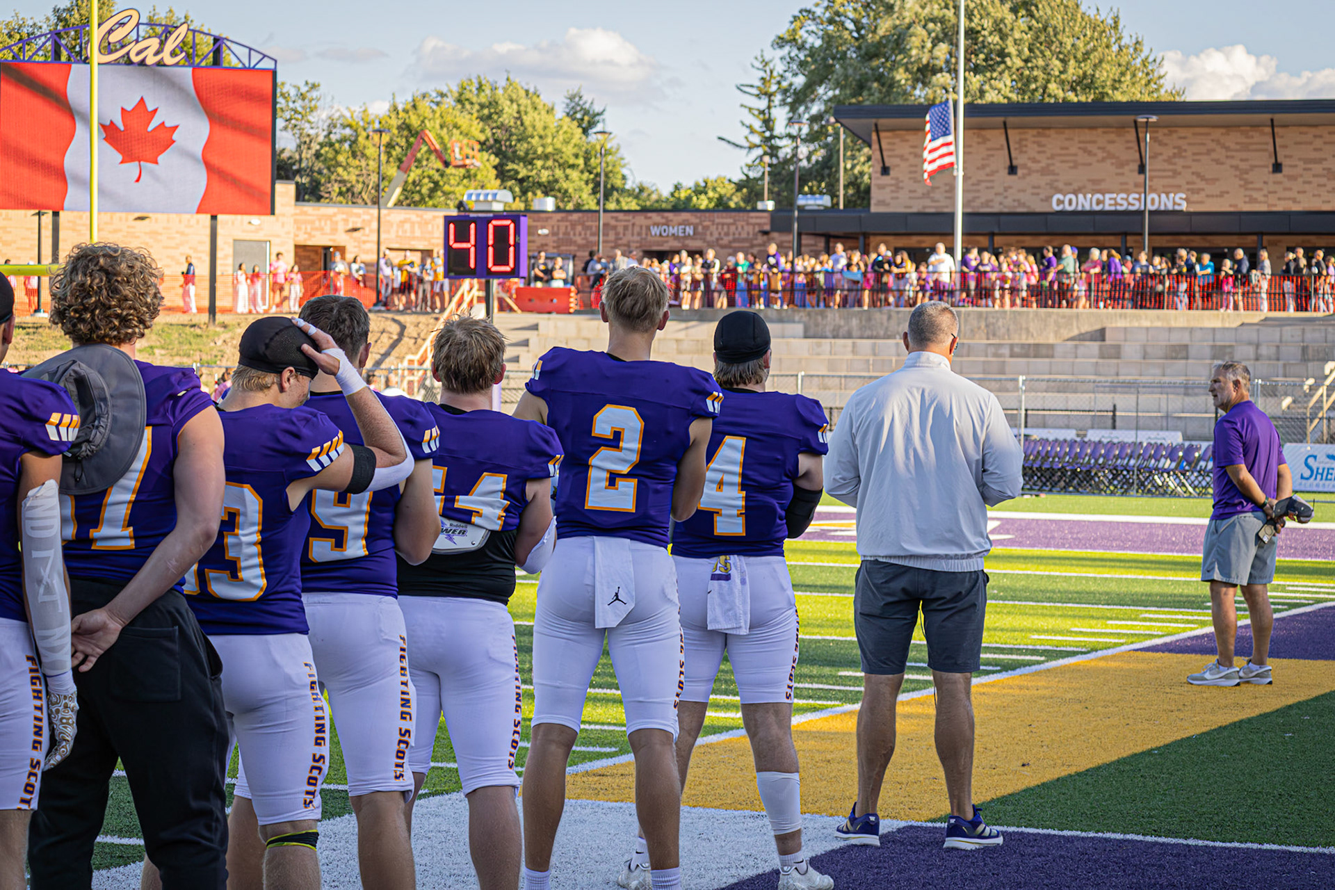 Players and fans pause for the national anthems before kickoff, united as the Canadian flag glows on the scoreboard and the American flag flies at half-staff.(Photo by Egan Otto)