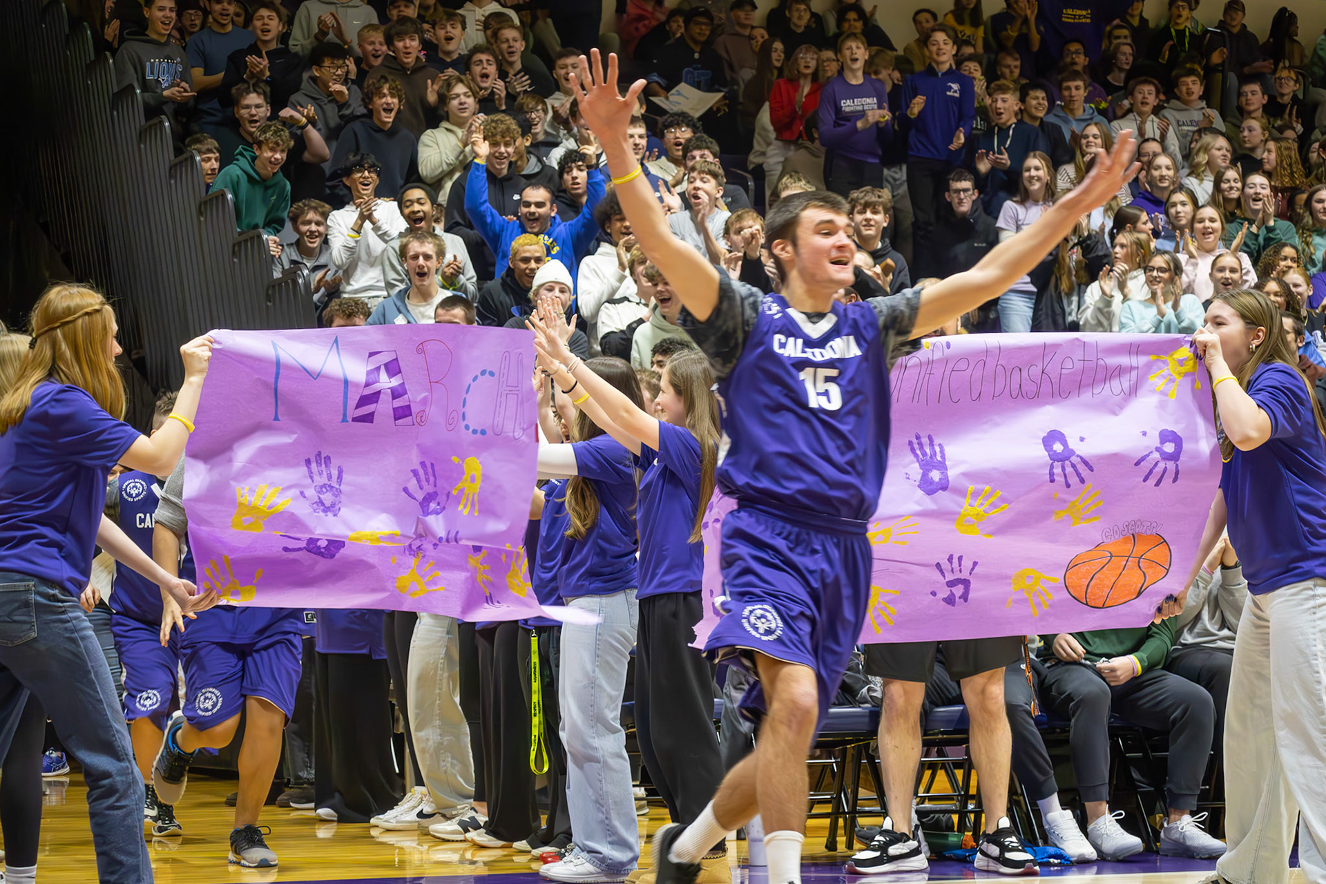 Unified player Josh Kietzman bursts through a paper banner to kick off the basketball game. (Photo by Avarey Lippert)