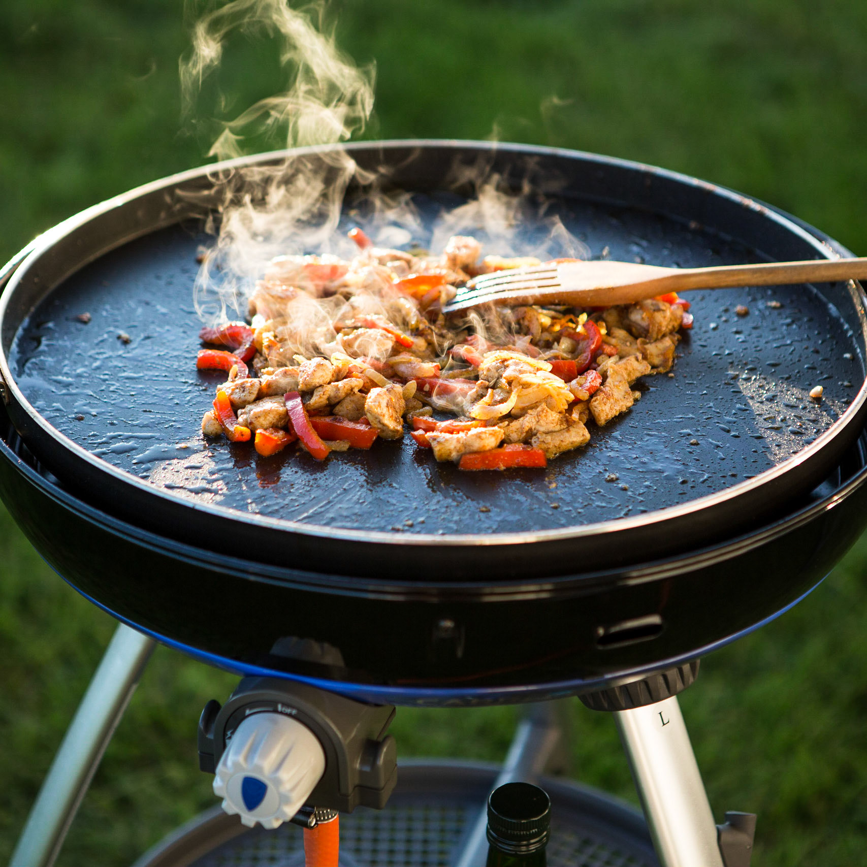 Food is cooking on a plate of a gas grill.