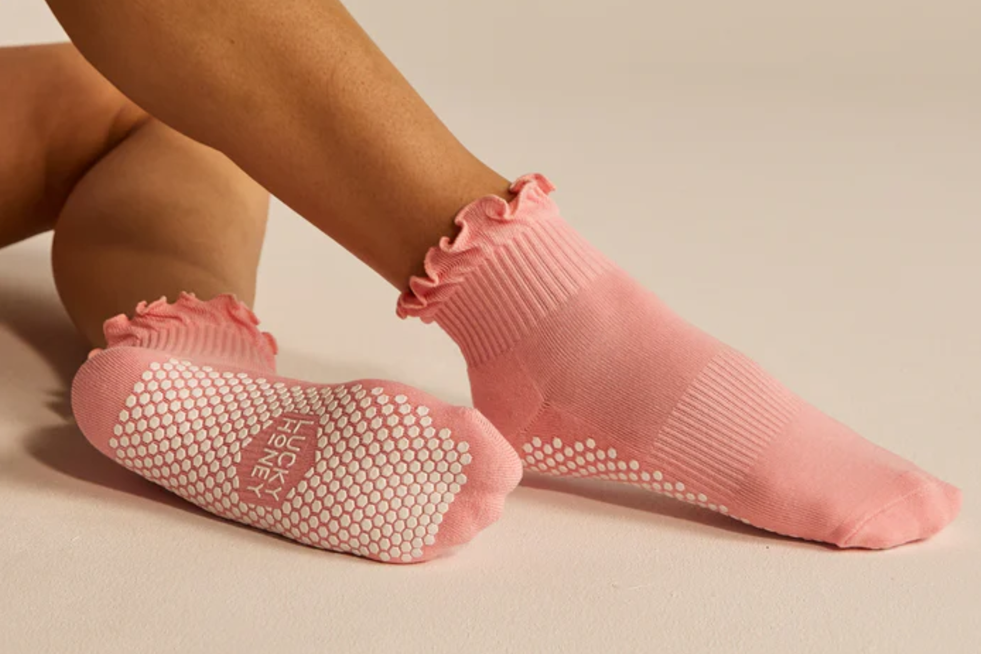 One pair of legs with Lucky Honey grapefruit orange ruffle grip socks on with the bottom of one sock showing the grippy dots and brand name