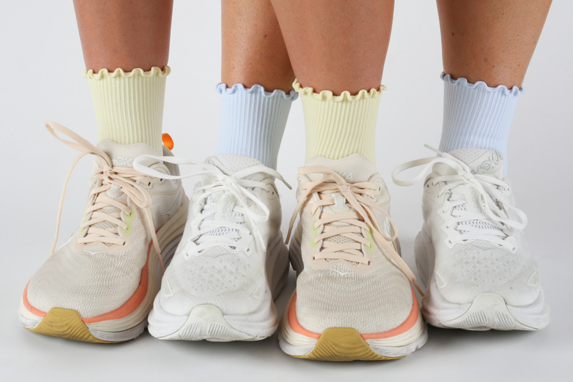 Two pairs of legs shown both wearing Saturday Strides quarter ruffle socks, one in yellow socks with off-white sneakers and the other in blue socks with white sneakers