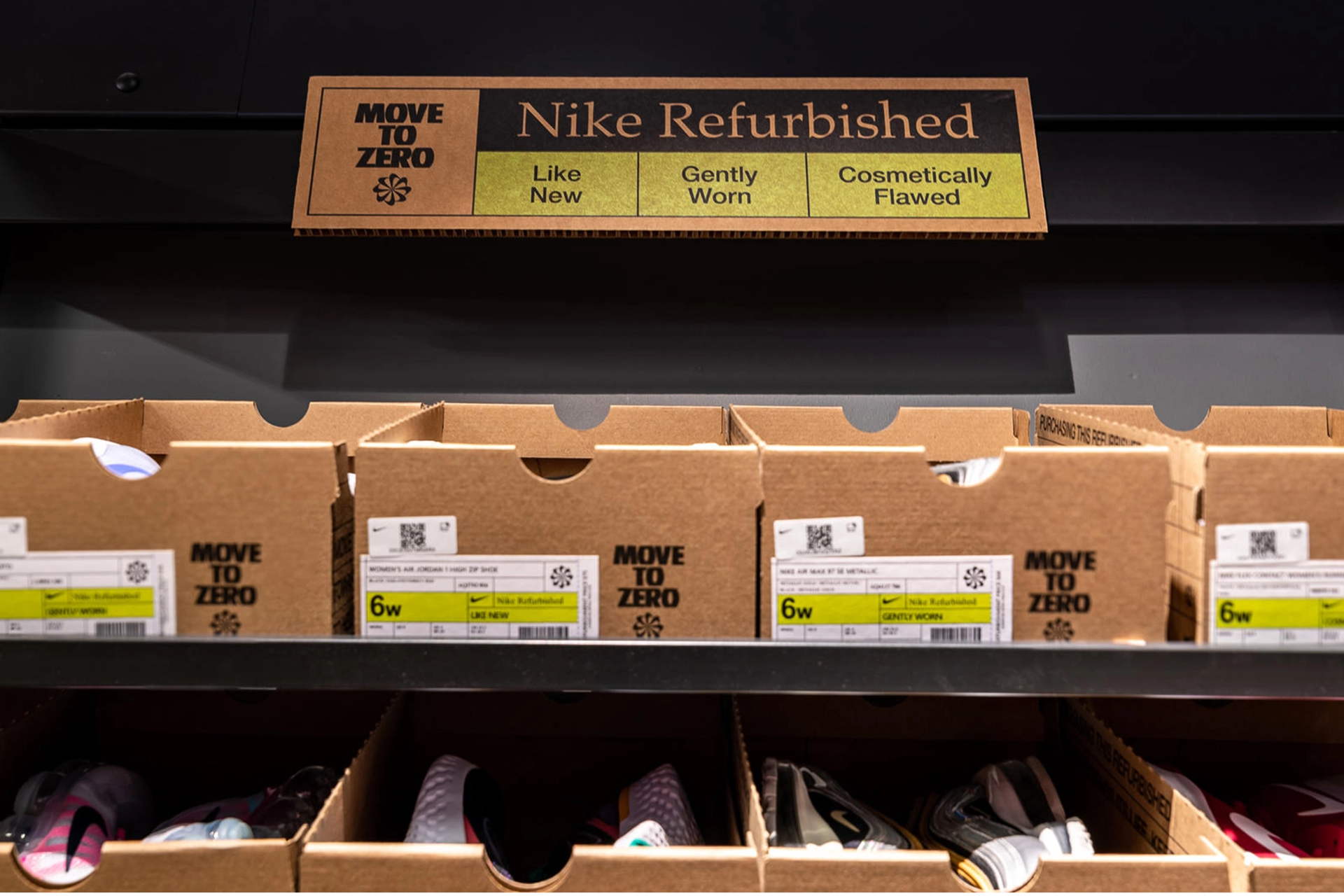Open Nike brown shoeboxes displayed on shelves underneath a sign for the Nike Refurbished program with “Like New”, “Gently Worn”, and “Cosmetically Flawed” as options for sorting.