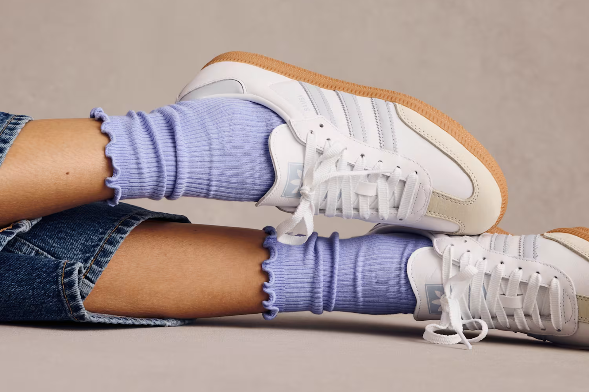 A pair of legs with jeans, blue Bombas half calf ruffle rib socks, and white sneakers on