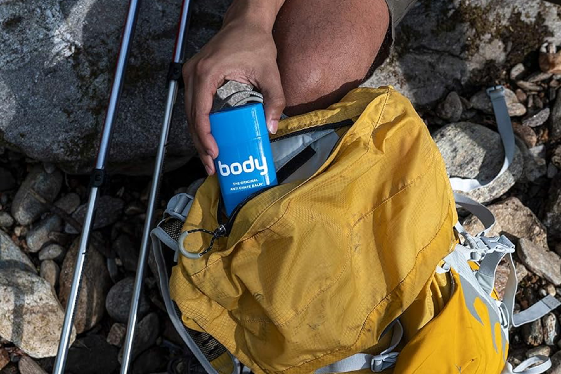 Man removing the blue Body Glide tube from his yellow hiking backpack next to trekking poles