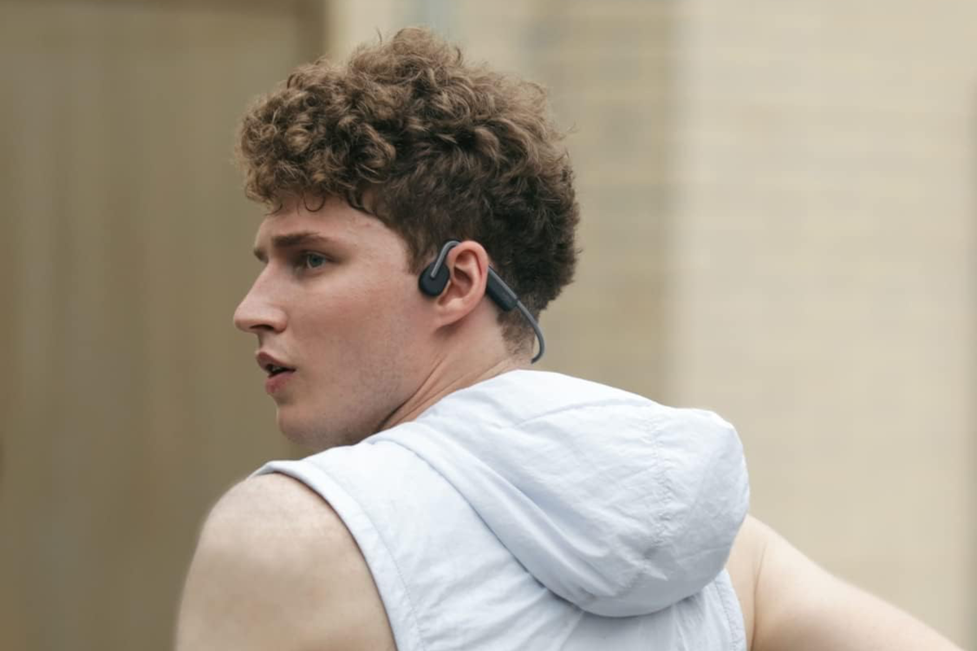 Man running and looking to his left side wearing black Shokz open-ear headphones